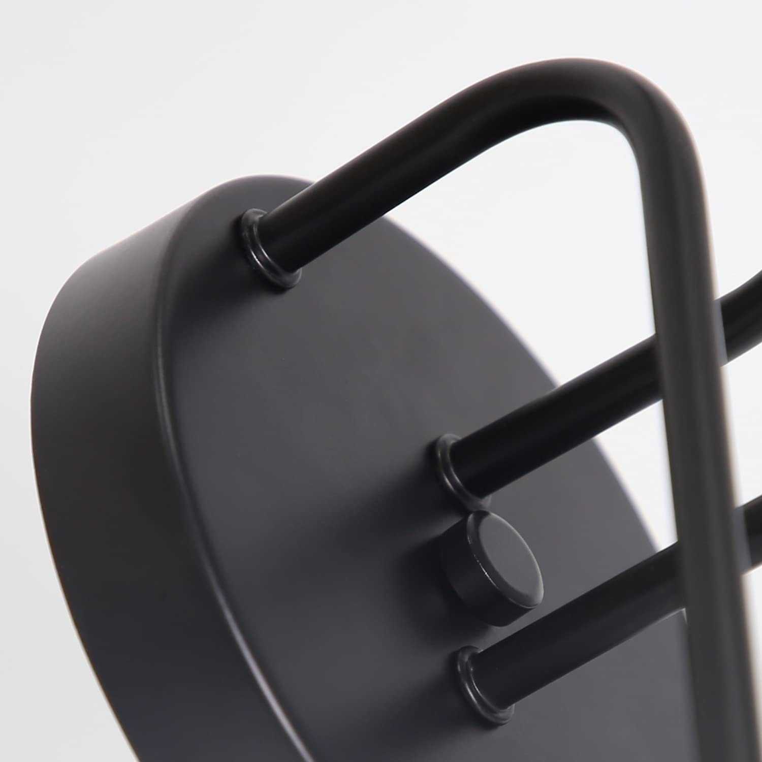 Zbliżenie czarnego, okrągłego metalowego elementu oprawy oświetleniowej z zakrzywionymi prętami wspornikowymi.