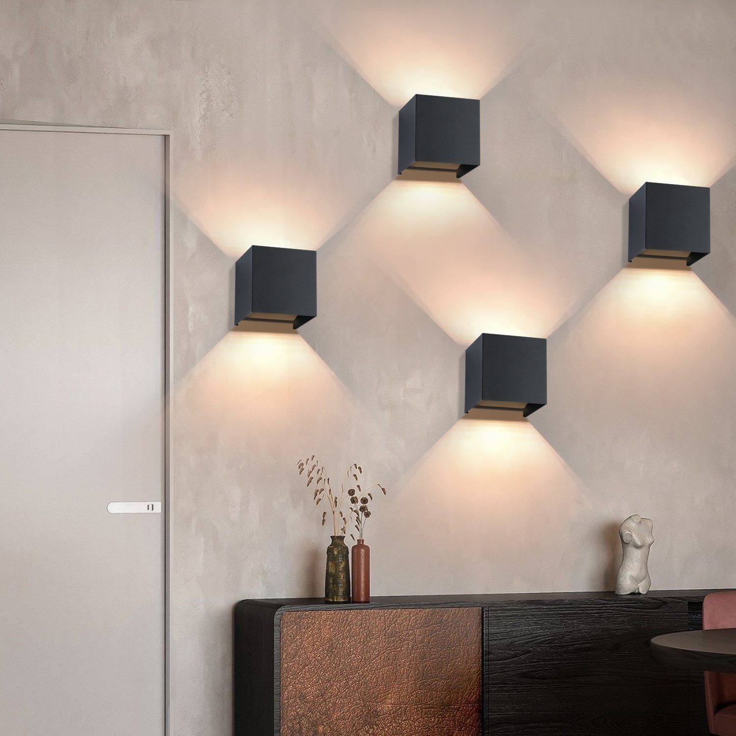 Quattro lampade da parete nere a forma di cubo sono montate su un muro. Proiettano la luce verso il basso. Un mobile sottostante.