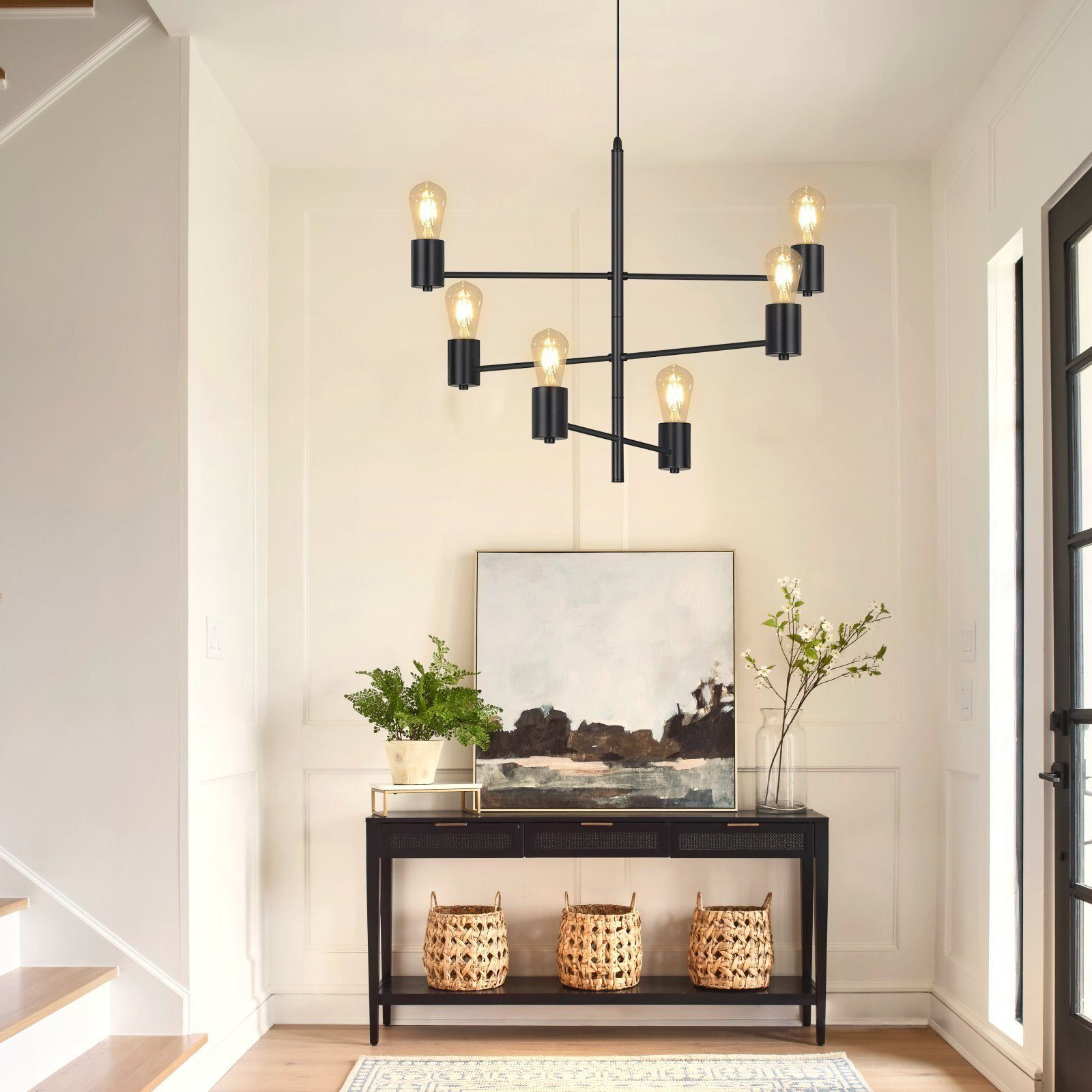 Czarny żyrandol wisi w korytarzu. Konsola ma sztukę, kosze i rośliny. Widoczne są białe ściany i drzwi.