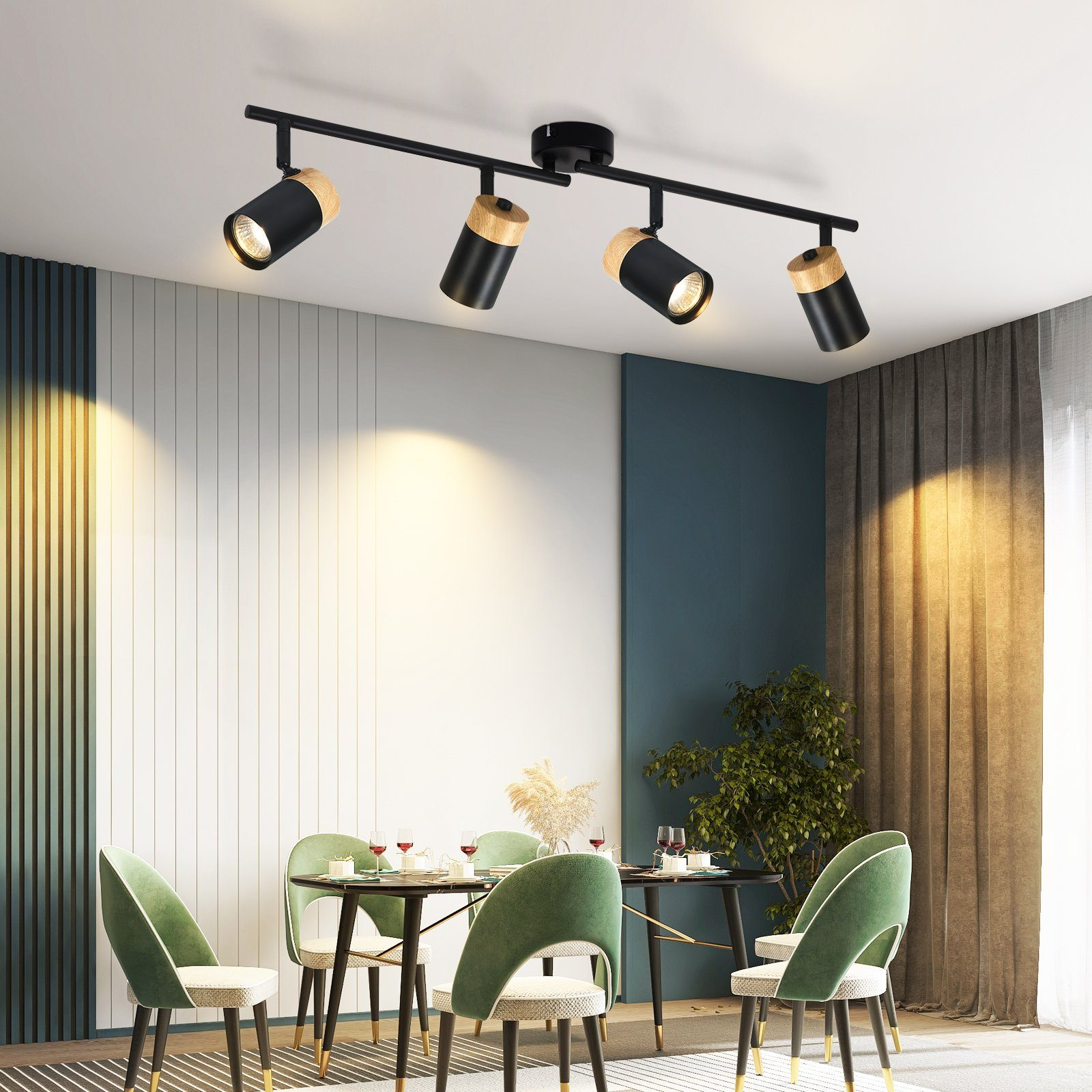 Quattro faretti neri e in legno illuminano un tavolo da pranzo apparecchiato, sedie verdi.