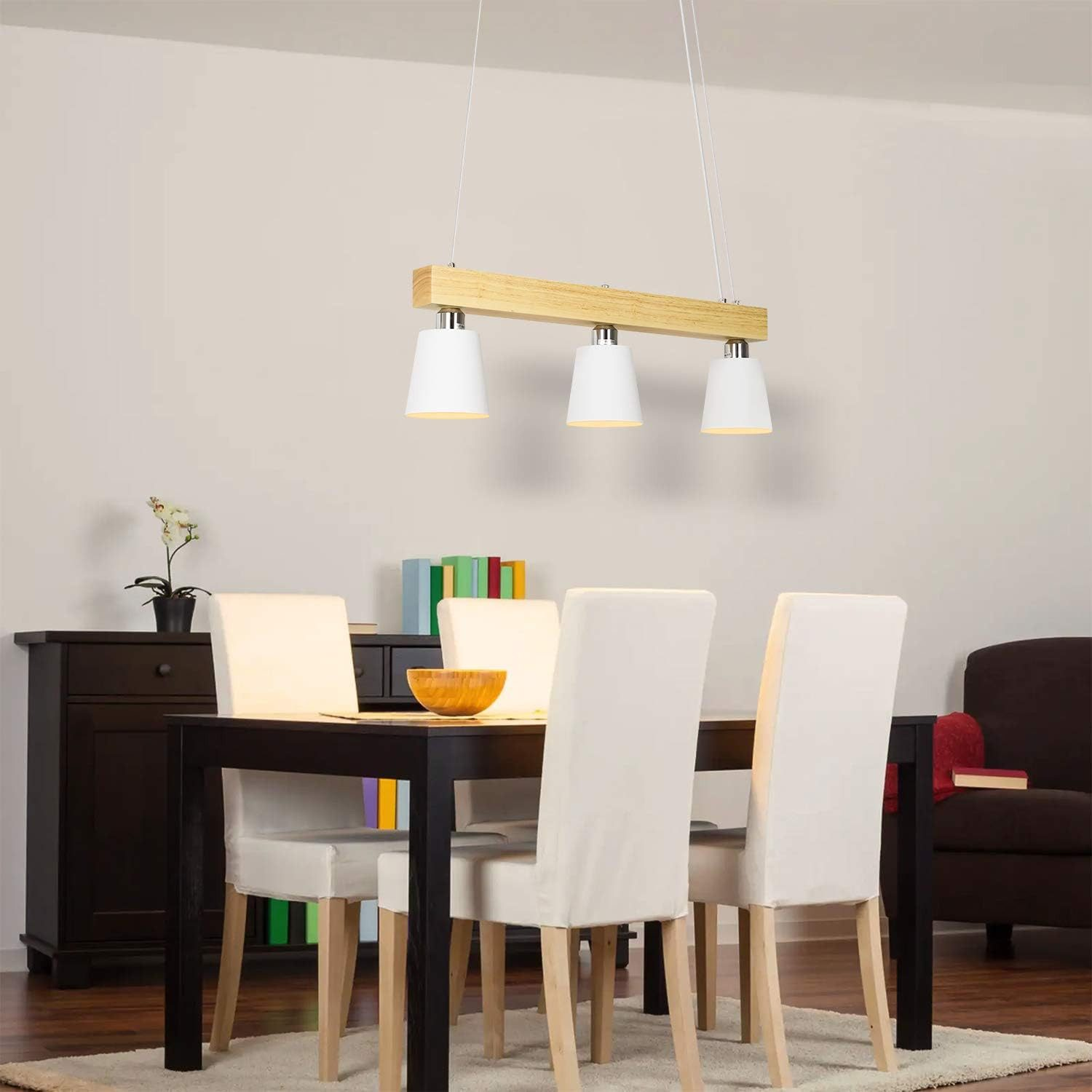 Una sala da pranzo con tavolo in legno, sedie bianche e una lampada a sospensione a tre luci.