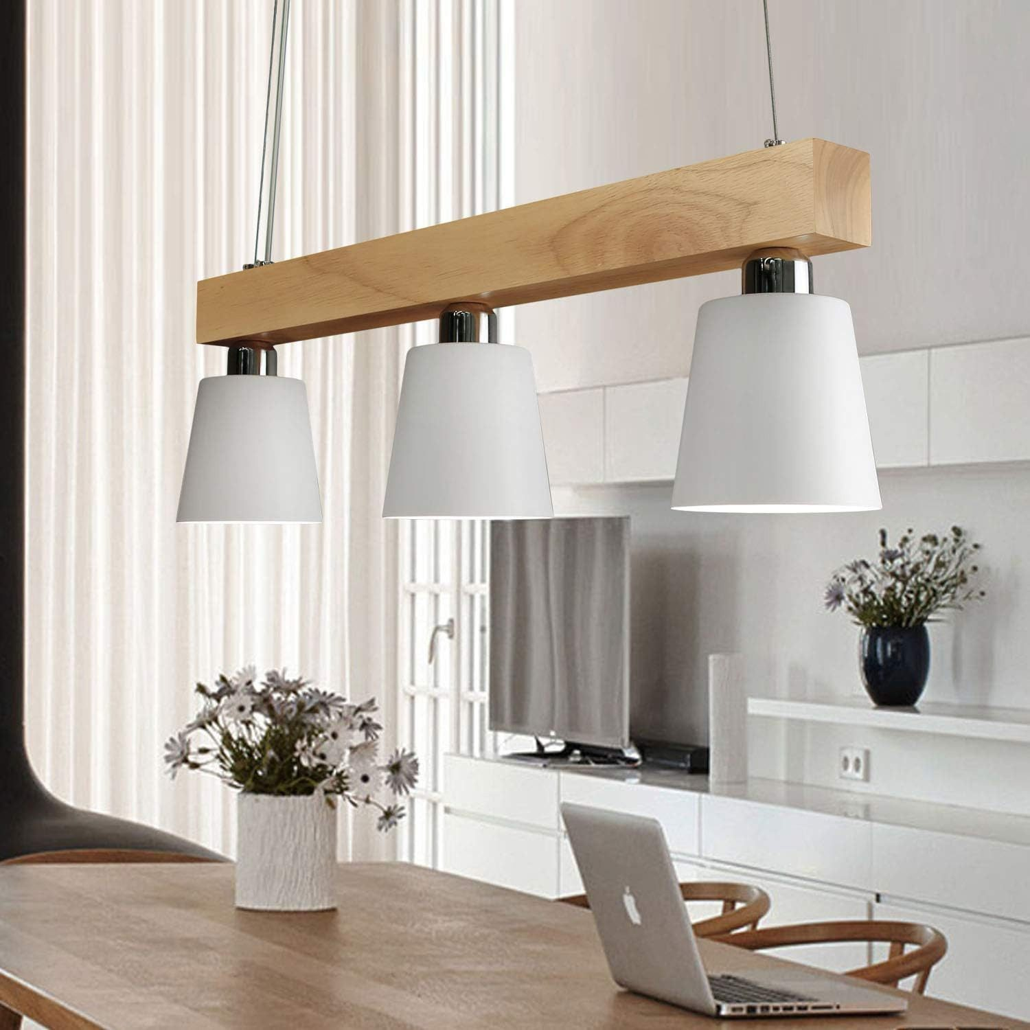Una sala da pranzo con lampade a sospensione sopra il tavolo. Tre lampade bianche a forma di cono con trave in legno.