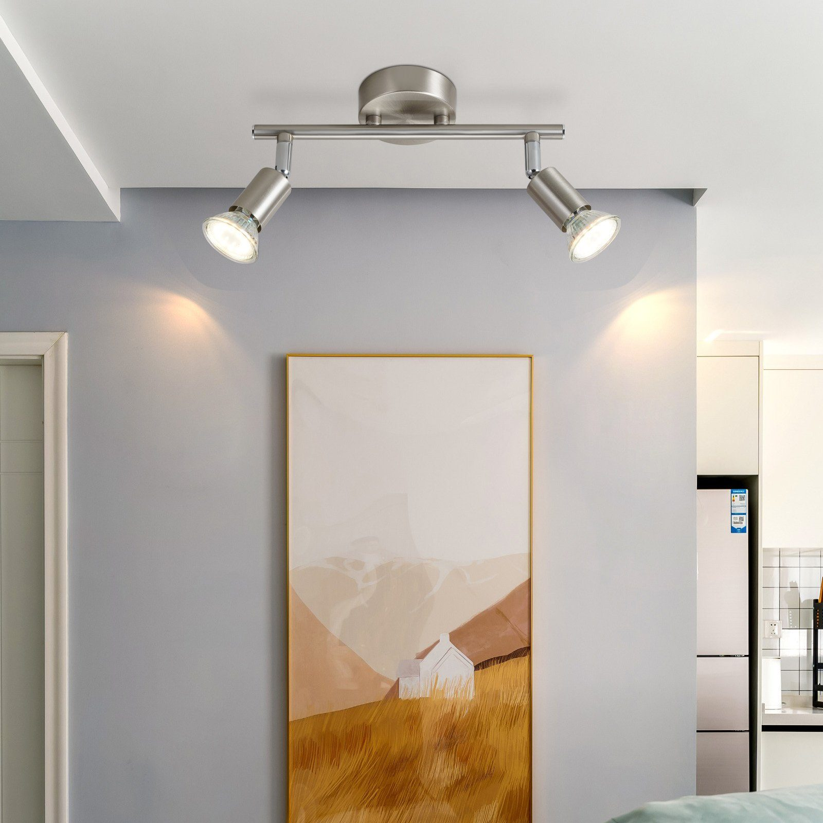 Dwa srebrne reflektory na szarej ścianie, oświetlające dzieło sztuki.