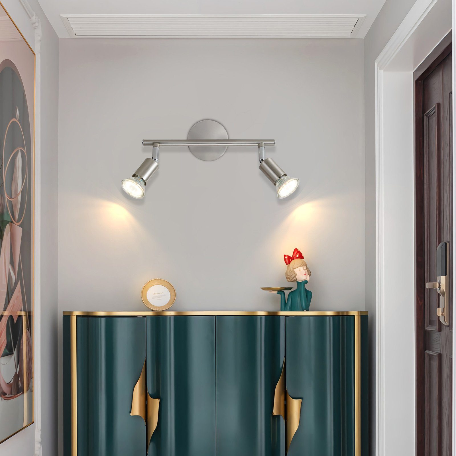 Korytarz z dwoma reflektorami nad szafką z dekoracją. Obraz na ścianie po lewej stronie.