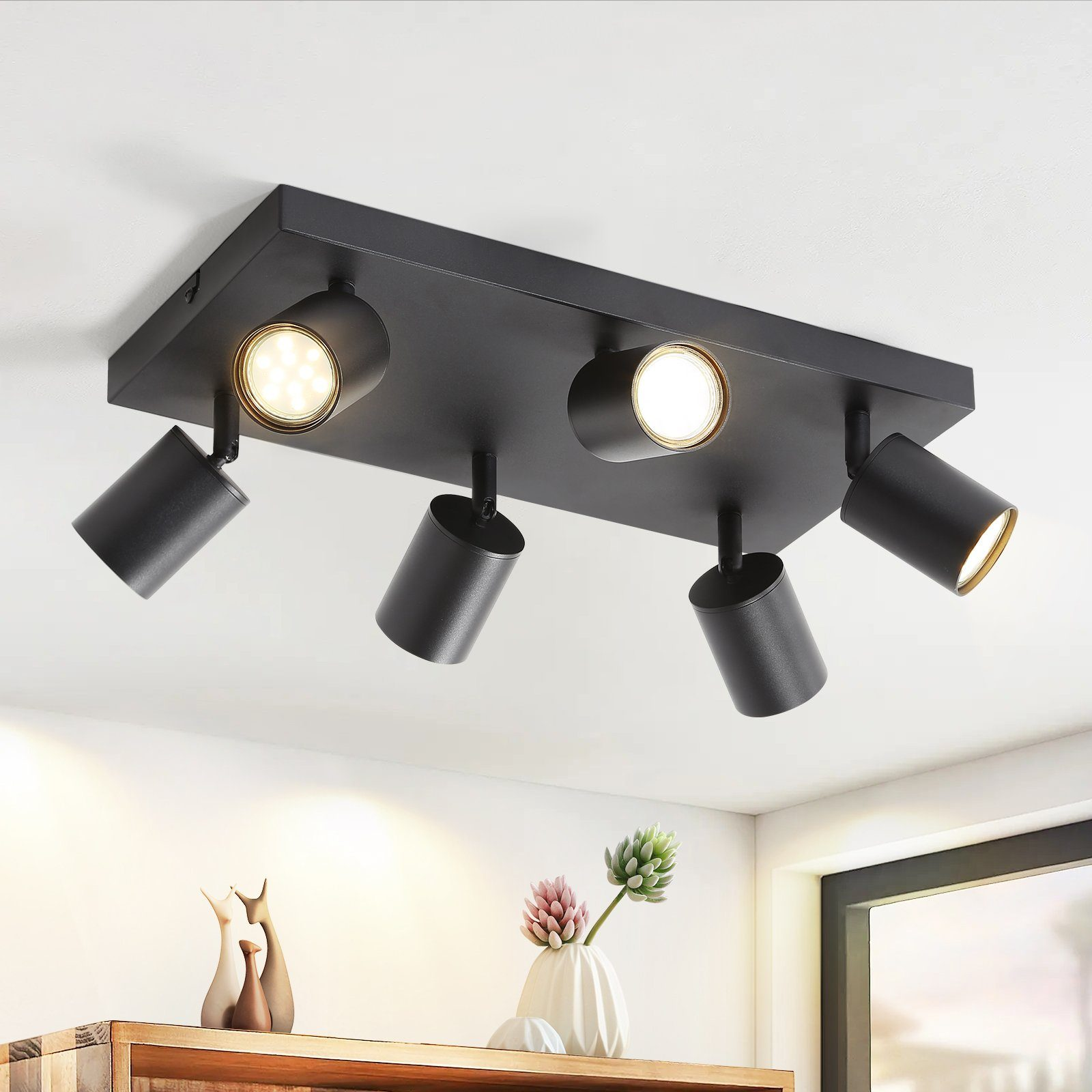 Un apparecchio di illuminazione a soffitto nero con quattro faretti orientabili, montato su un soffitto bianco.