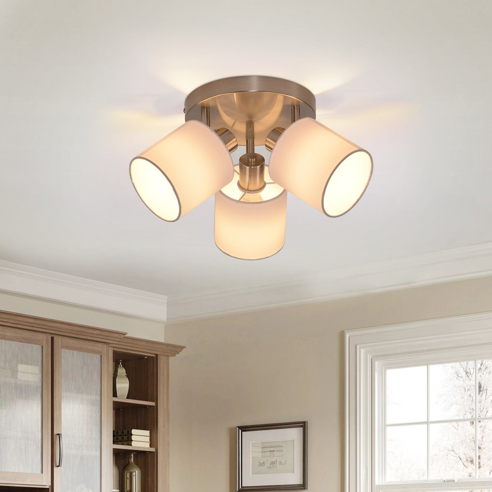 Lampa sufitowa z trzema białymi abażurami. Srebrne mocowanie. Światło jest włączone. Beżowa ściana. Biały sufit.
