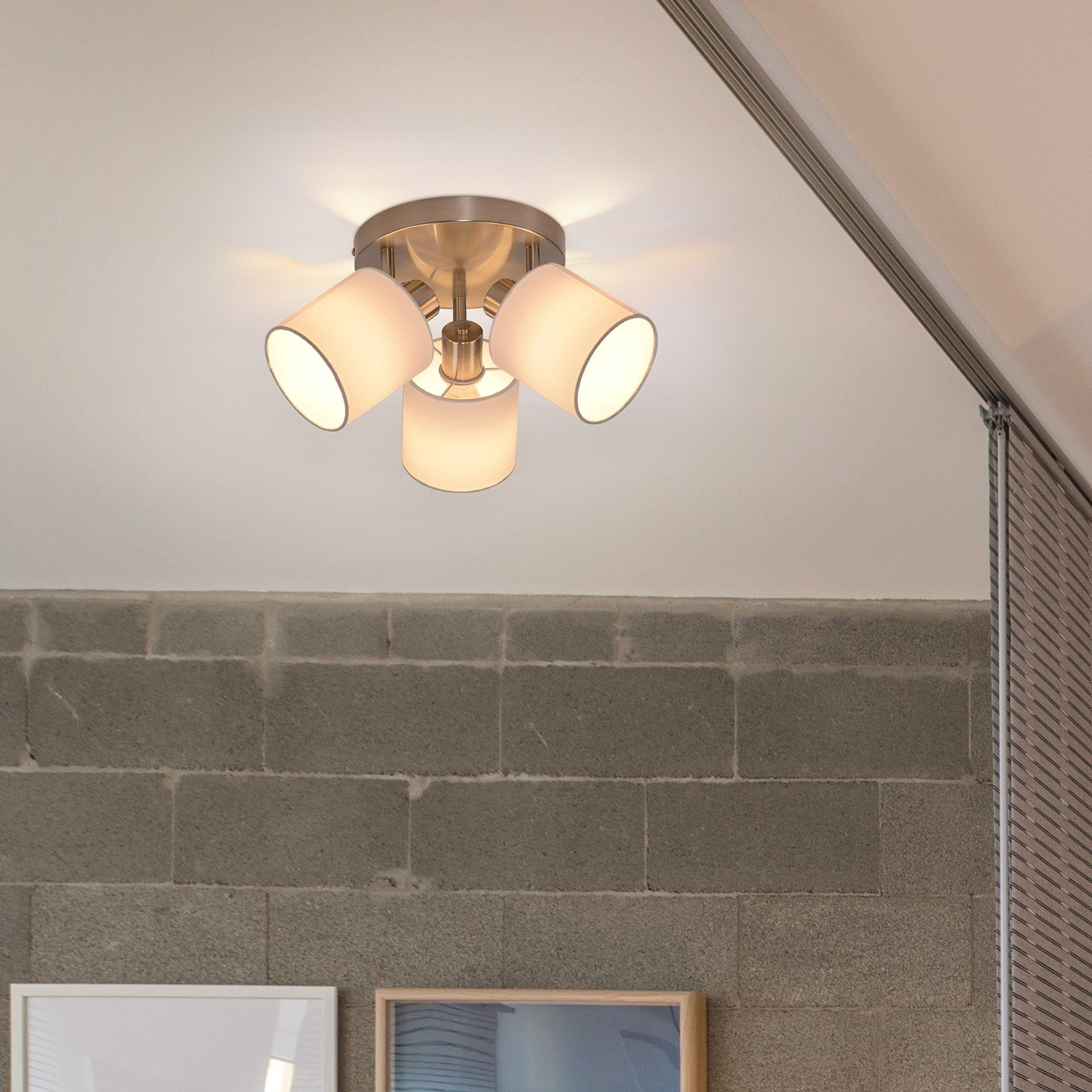 Lampa sufitowa z trzema abażurami. Widoczna szara ceglana ściana i rama obrazu.