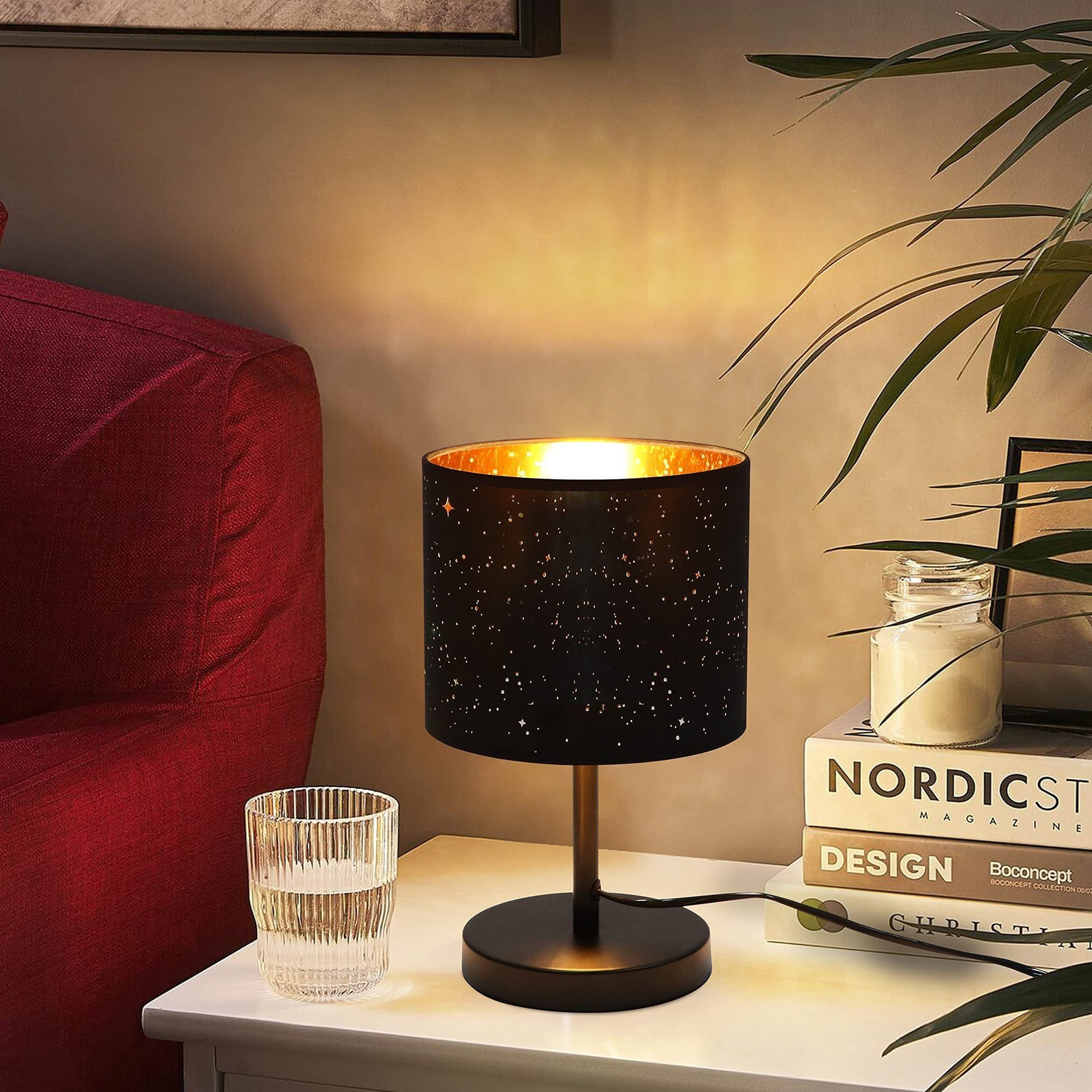 Czarna lampa z gwiaździstym kloszem i szklanka wody na białym stole. Czerwona sofa w tle.