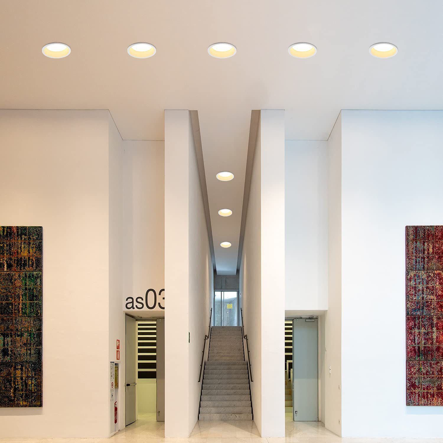 Flur mit weißen Wänden, Einbauleuchten und Kunst. Treppen führen nach oben.