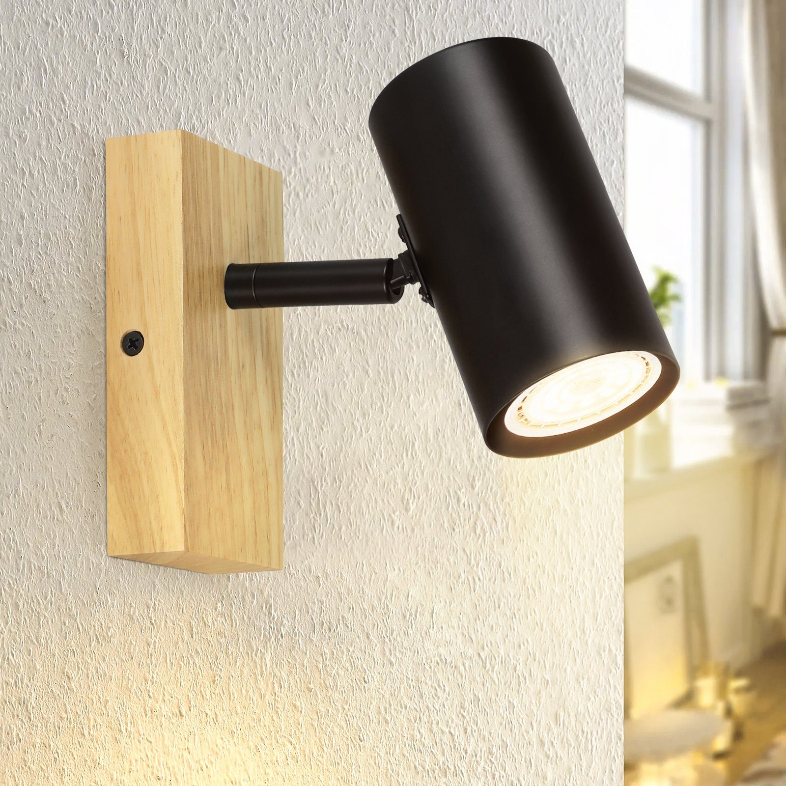 Eine schwarze, zylindrische Wandleuchte auf Holzsockel. Sie beleuchtet die Wand darunter.