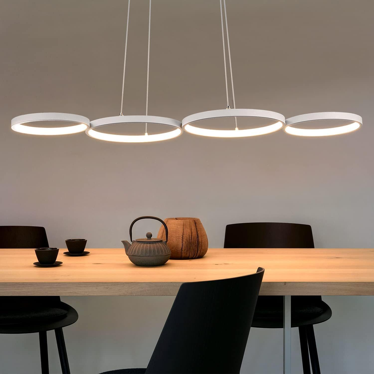 Una sala da pranzo con un tavolo in legno, lampade a sospensione moderne, sedie nere e oggetti decorativi.