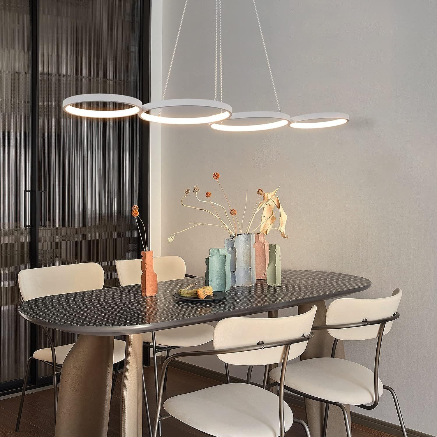 Sala da pranzo con un tavolo. Quattro luci circolari sono appese sopra. Vasi e cibo sono sul tavolo.