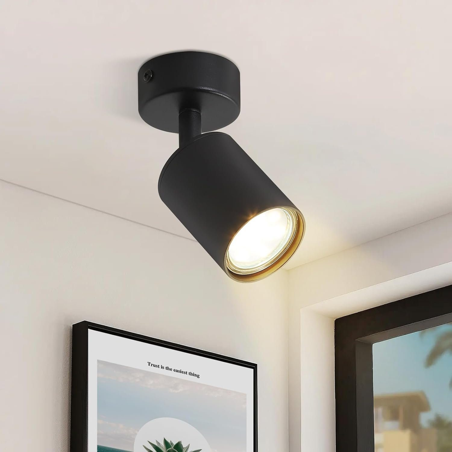 Un faretto nero è montato su un soffitto bianco, con un poster sottostante, che recita 'Trust is the easiest thing'.
