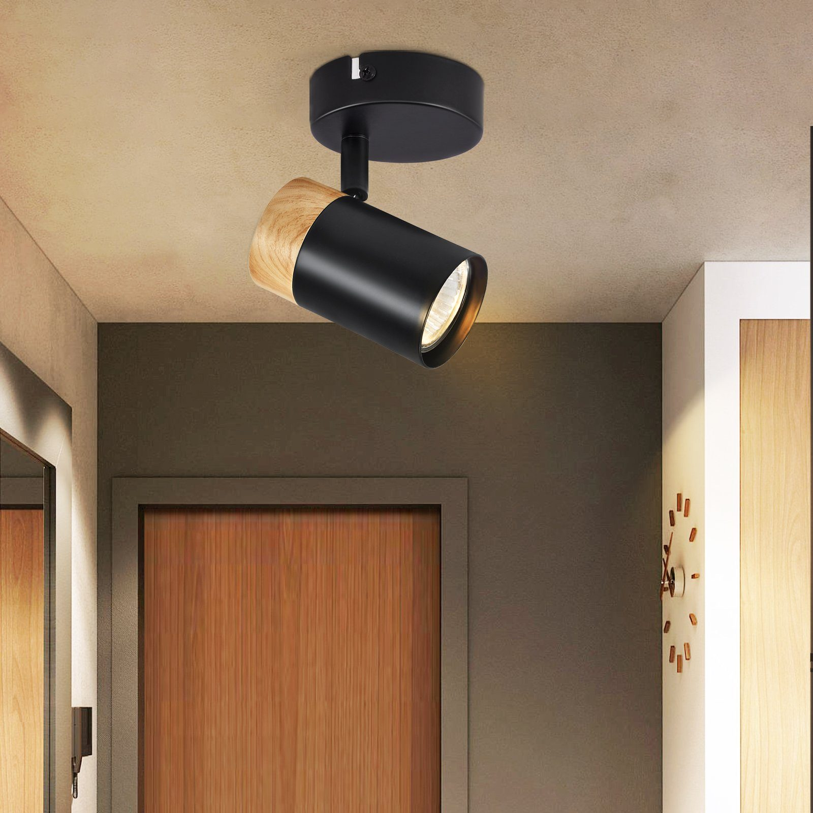 Faretto nero e legno a soffitto. Sfondo: porta e parete in legno, orologio. Luce calda.