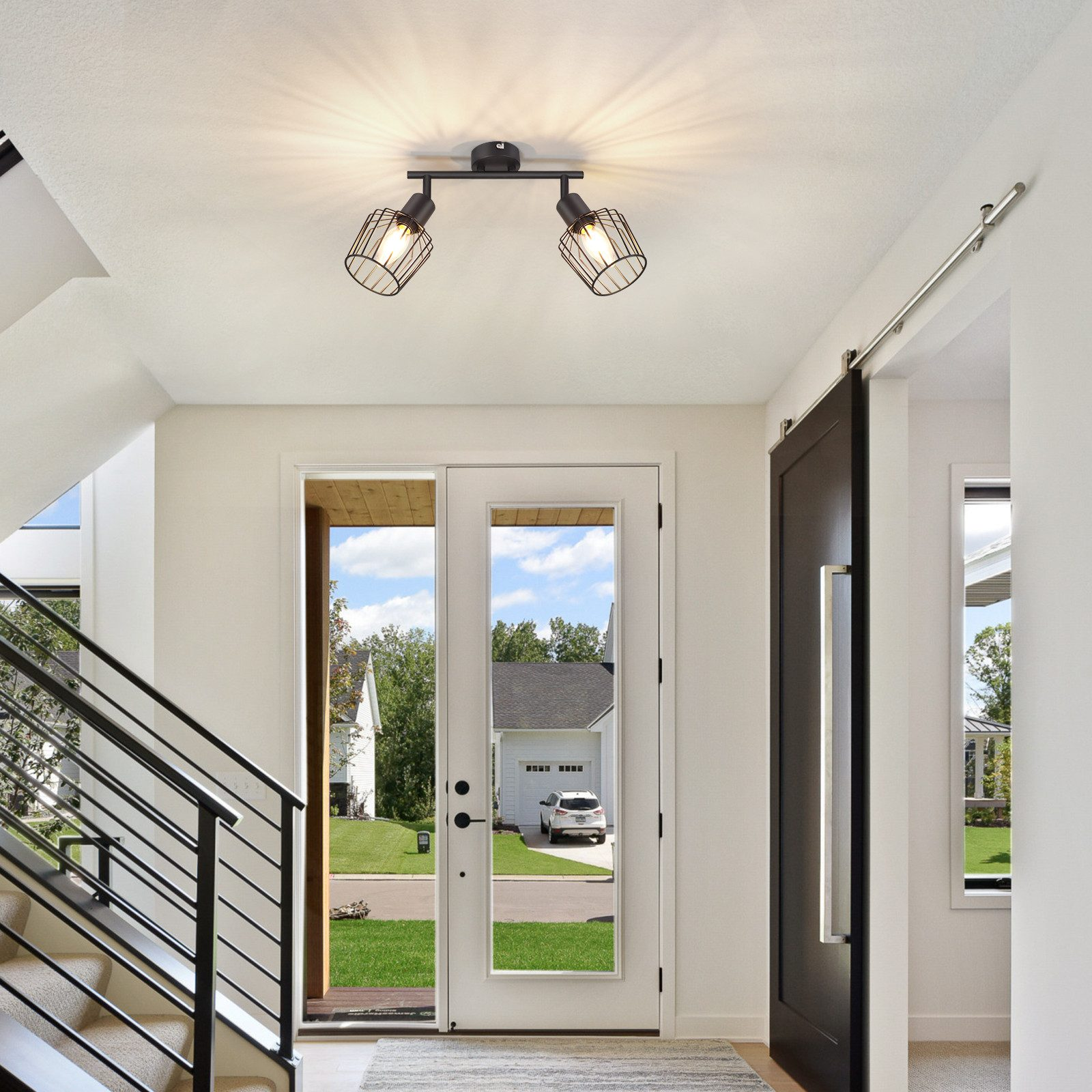 Ingresso con pareti bianche, scale, porta nera e due luci nere sul soffitto.