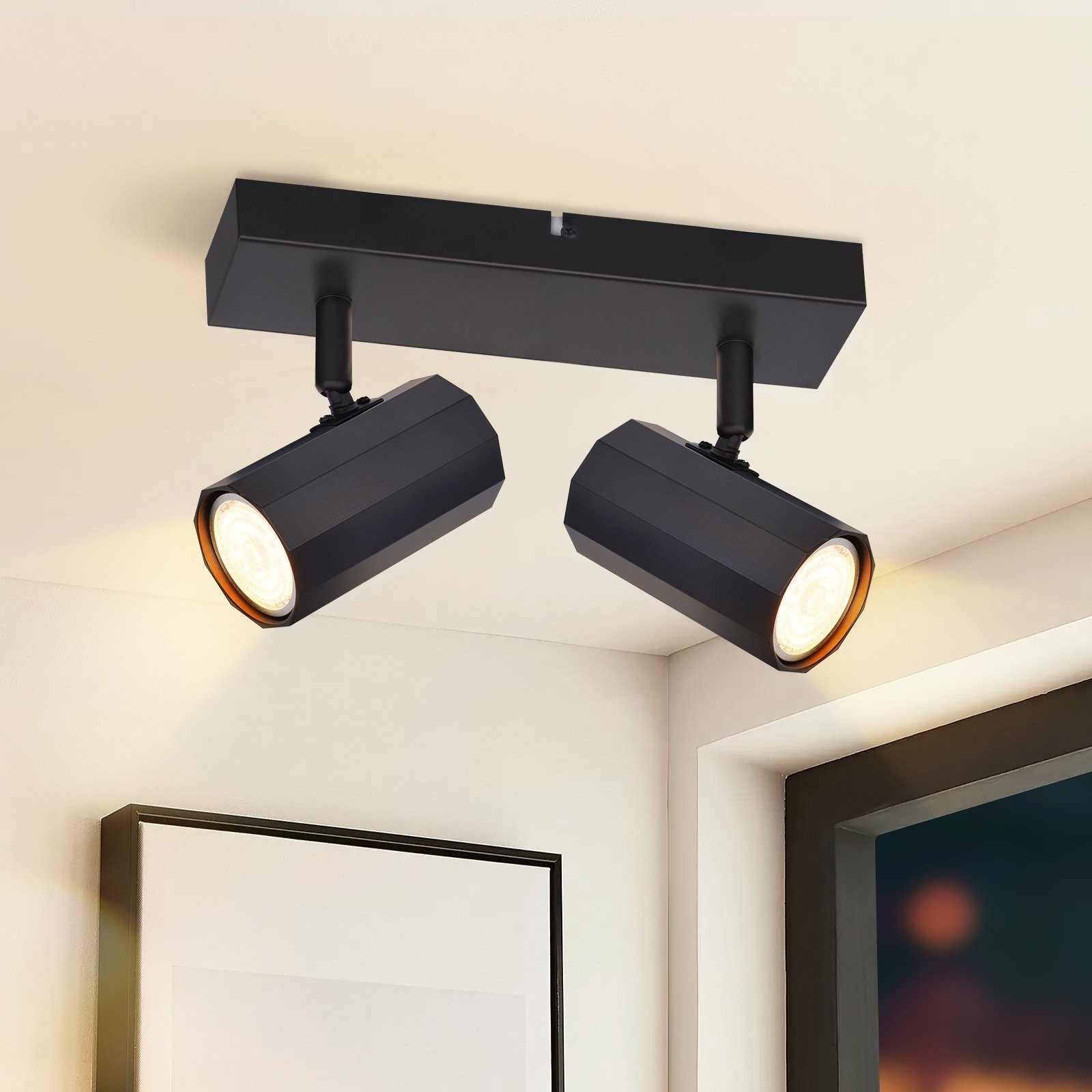Due faretti neri con lampadine su un soffitto bianco, angolati per illuminare un'area.