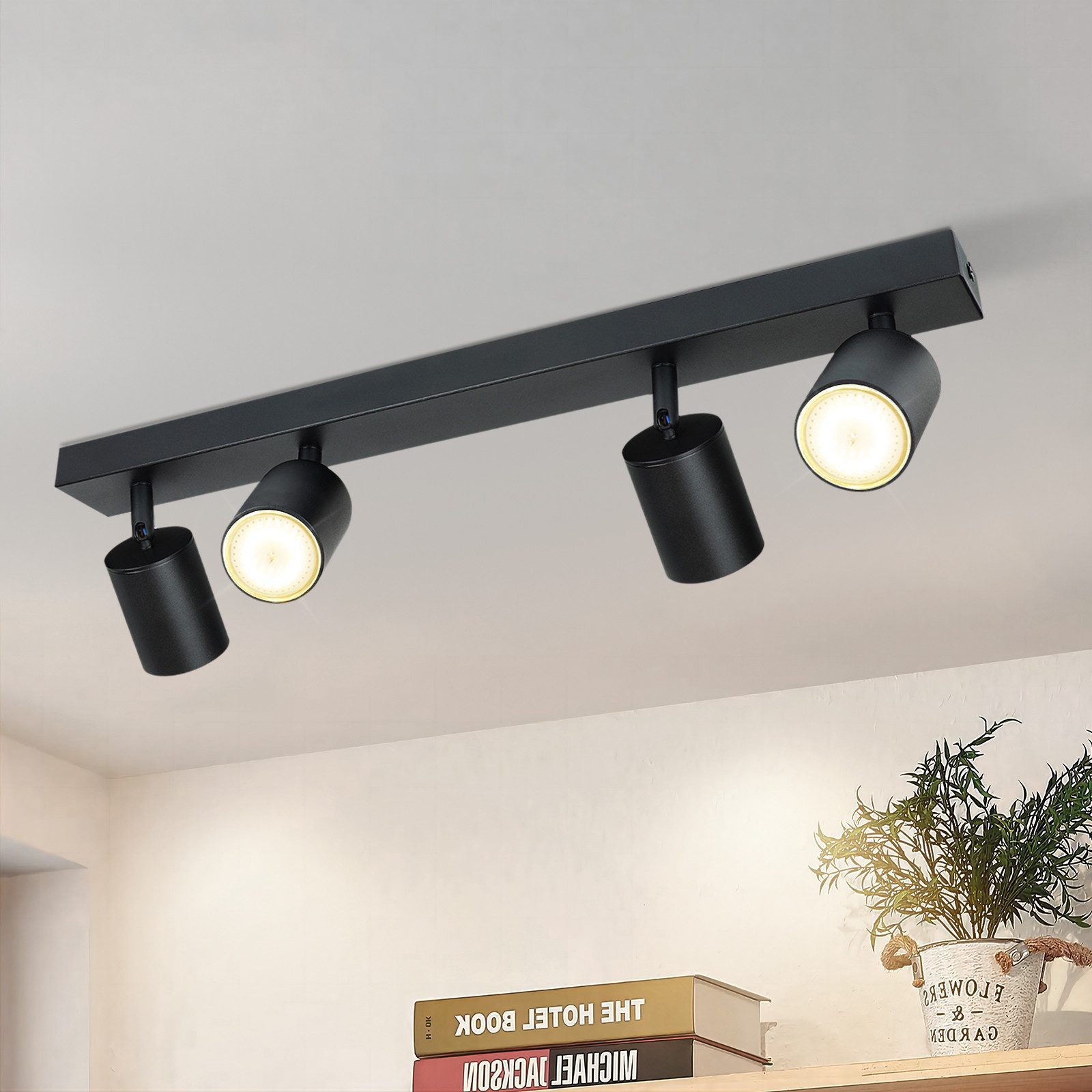 Faretto nero da soffitto con quattro luci. La luce è intensa. Lo sfondo è il soffitto e delle piante.