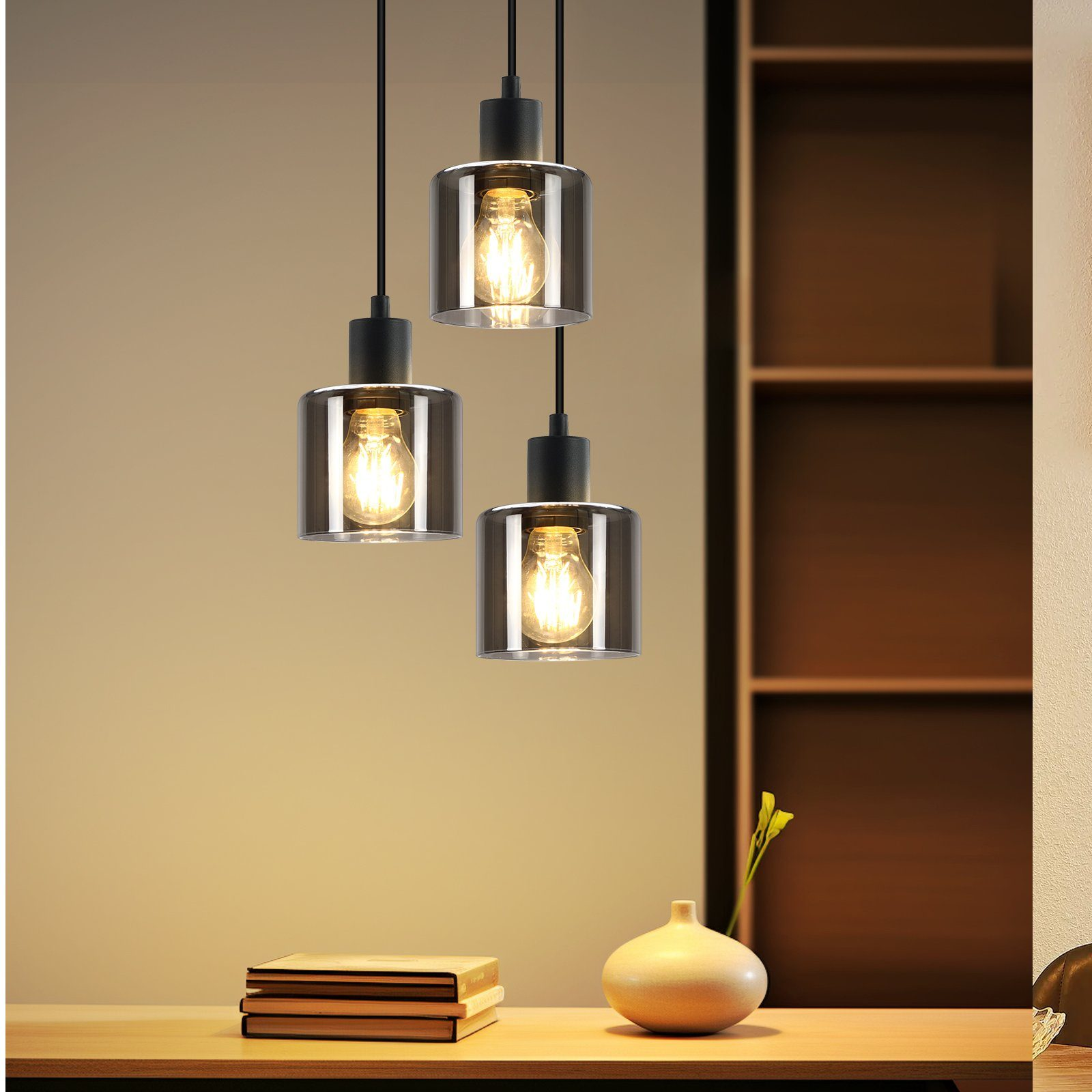 Drei Hängeleuchten mit Glasschirmen über einem Tisch. Die Lichter sind an und beleuchten den Bereich.