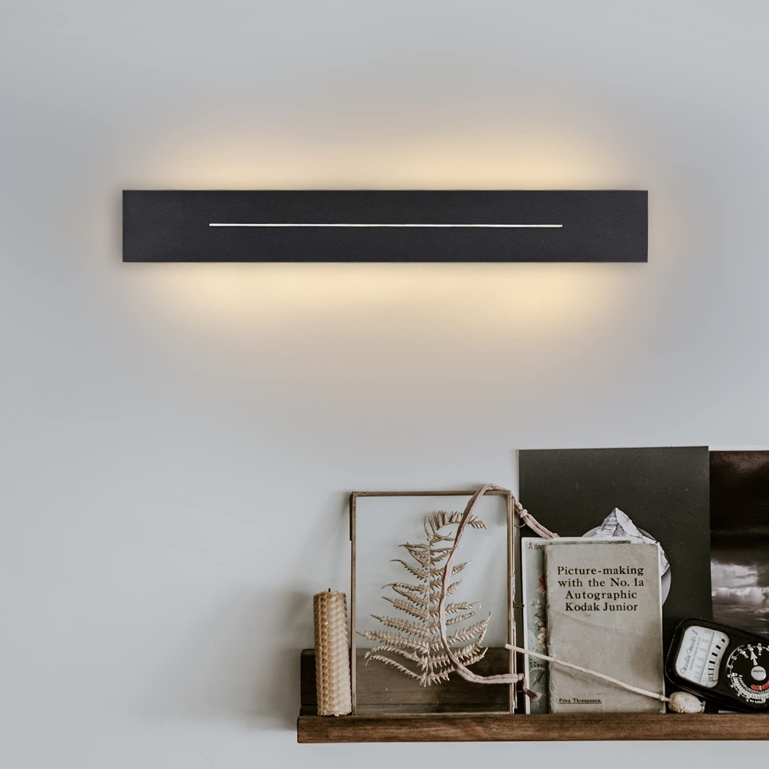 Lampada da parete con cornice nera, linea di luce bianca e mensola in legno con decorazioni.