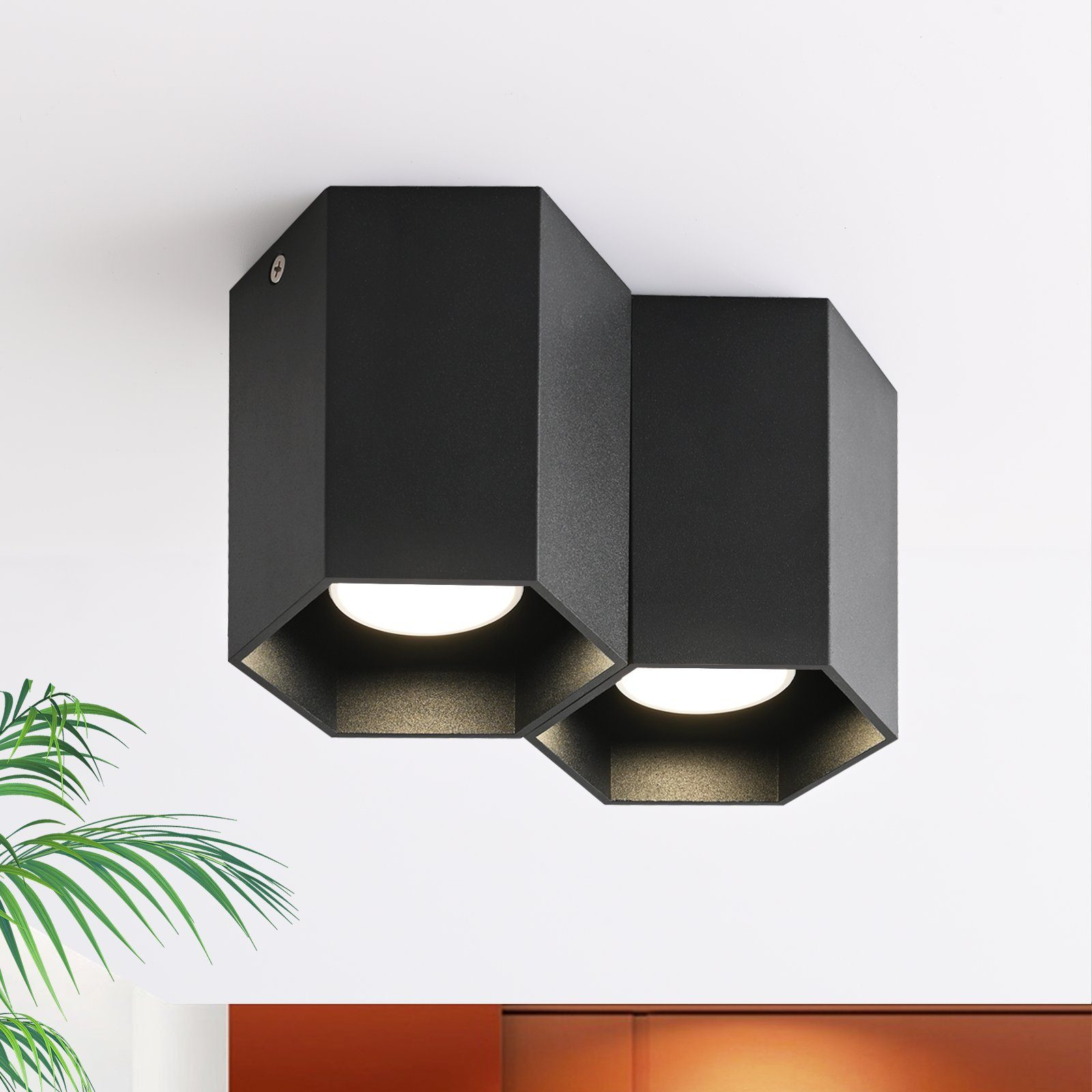 Due lampade da soffitto esagonali nere montate su un soffitto bianco. Le luci sono accese.
