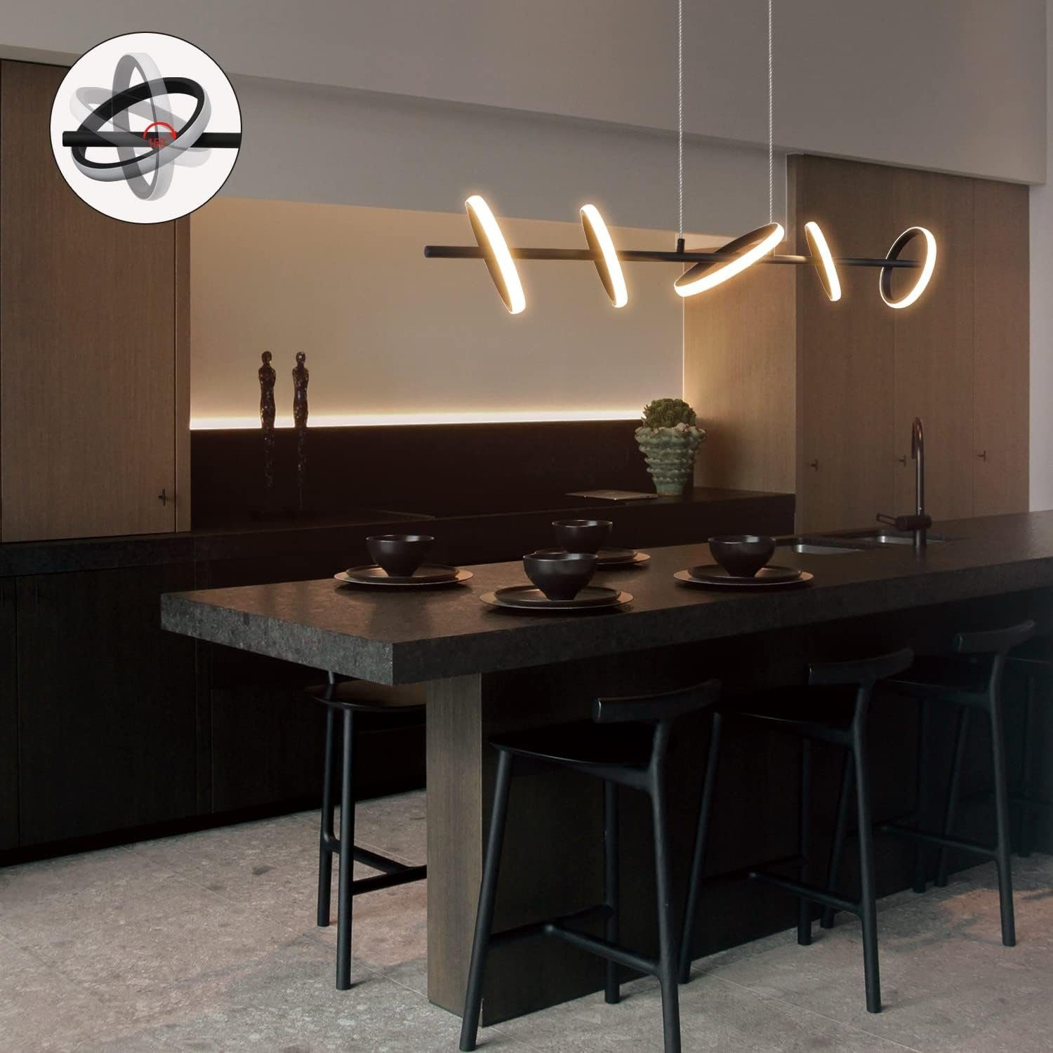 Cucina moderna con piano di lavoro nero e luci a sospensione. Sedie nere e sfondo dai toni neutri.