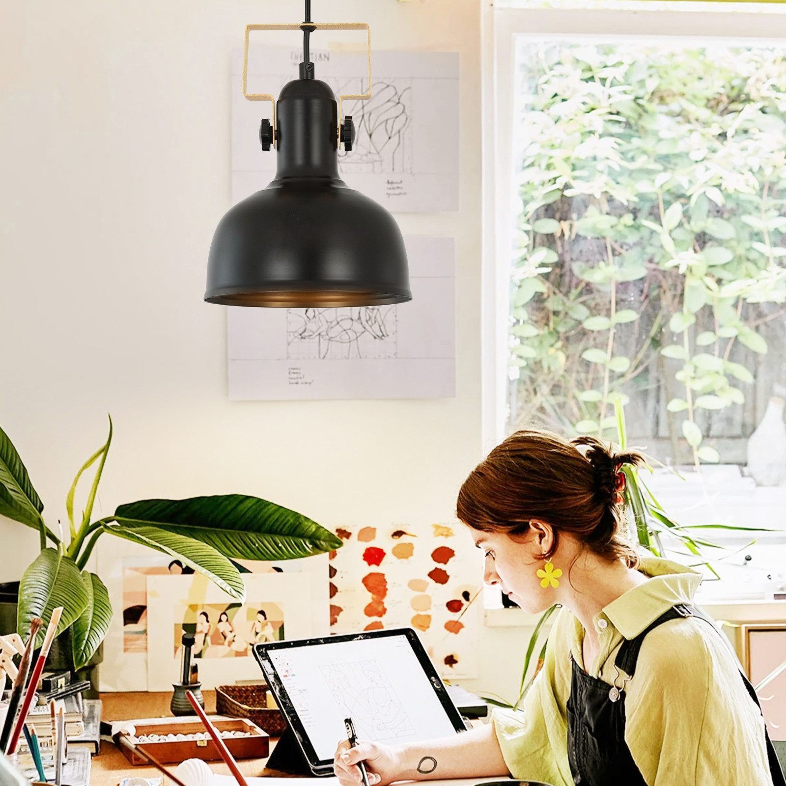 Kobieta szkicuje na tablecie, używając pióra. Czarna lampa wisząca wisi w studio.