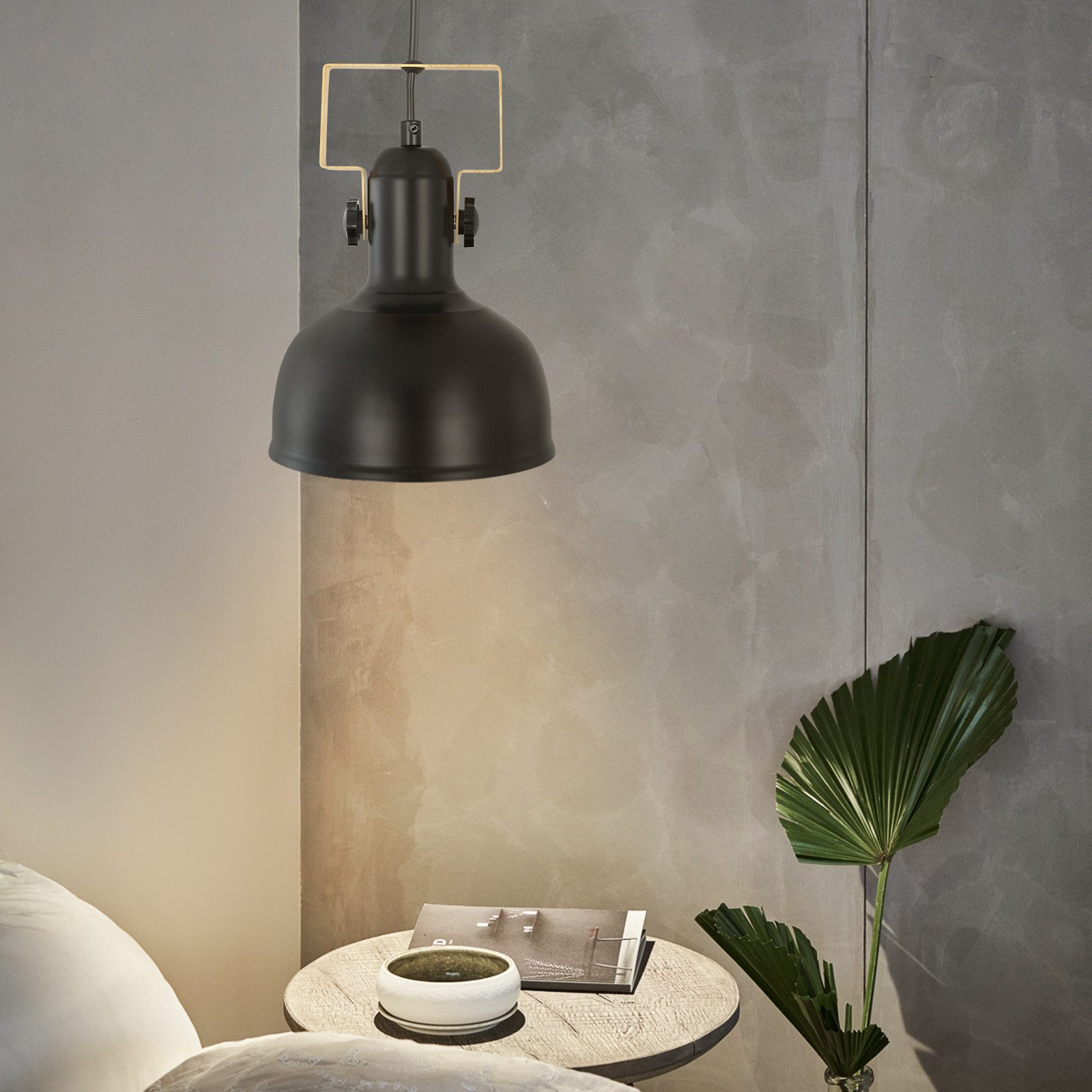 Czarna lampa wisząca w stylu vintage, nad stołem z dekoracjami i rośliną.