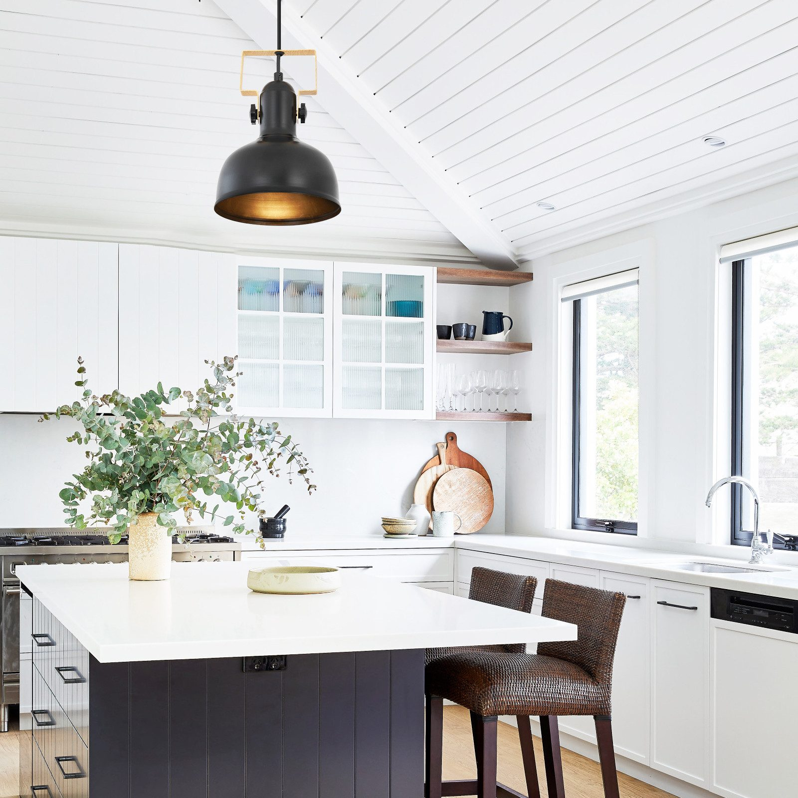 Kuchnia z lampą wiszącą i wyspą. Światło jest czarne, a wyspa biała i ciemna.