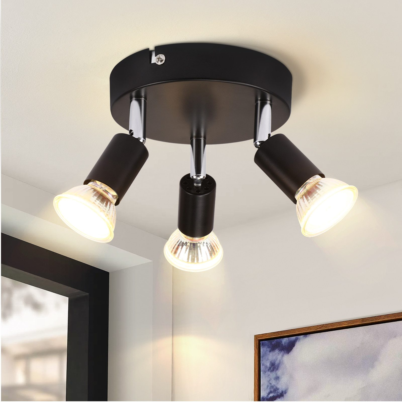 Lampada da soffitto con tre faretti neri orientabili. La stanza ha soffitto e pareti bianche.