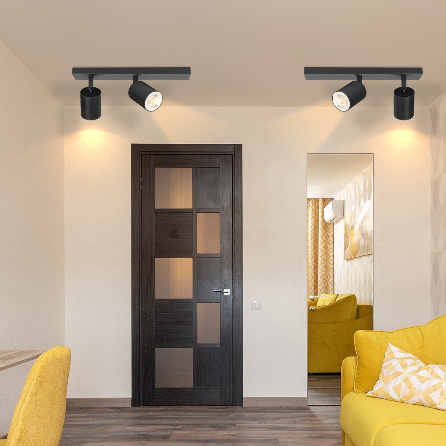 Illuminazione a binario nera con due faretti regolabili. L'ambientazione è una stanza con divano giallo e specchio.