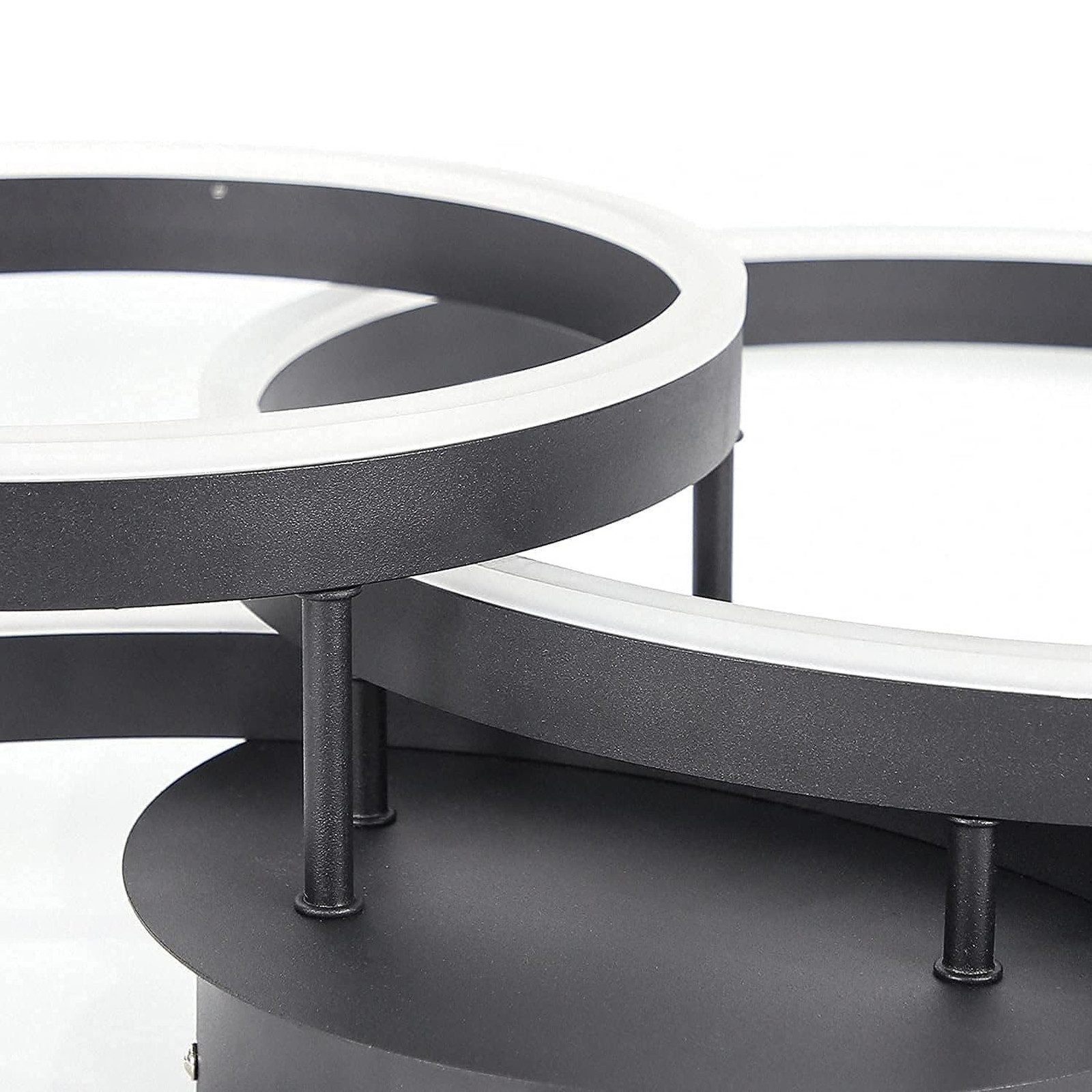 Primo piano di un lampadario nero e moderno. Mostra il design circolare con anelli bianchi illuminati.