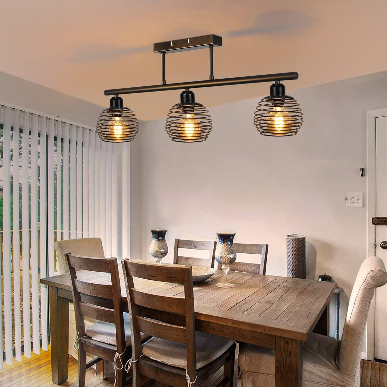 Sala da pranzo con tavolo in legno, sedie e tre lampade a sospensione. Lo sfondo mostra una finestra.