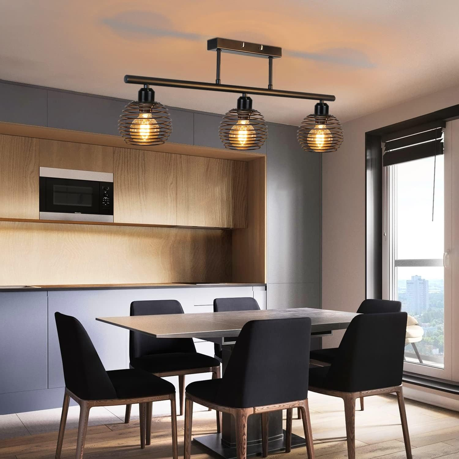 Lampada da soffitto con tre luci a gabbia di filo. Cucina con tavolo da pranzo. Sedie nere. Armadi in legno.