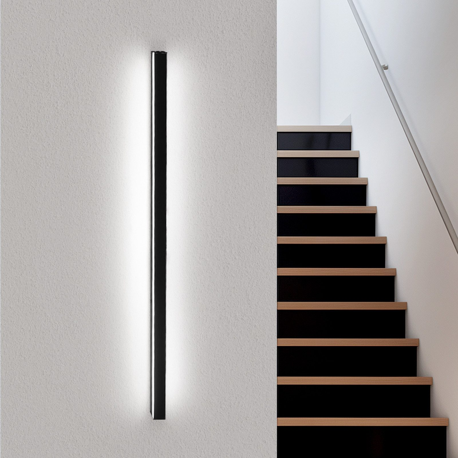 Un apparecchio di illuminazione a LED verticale nero su un muro bianco, vicino a una scala.