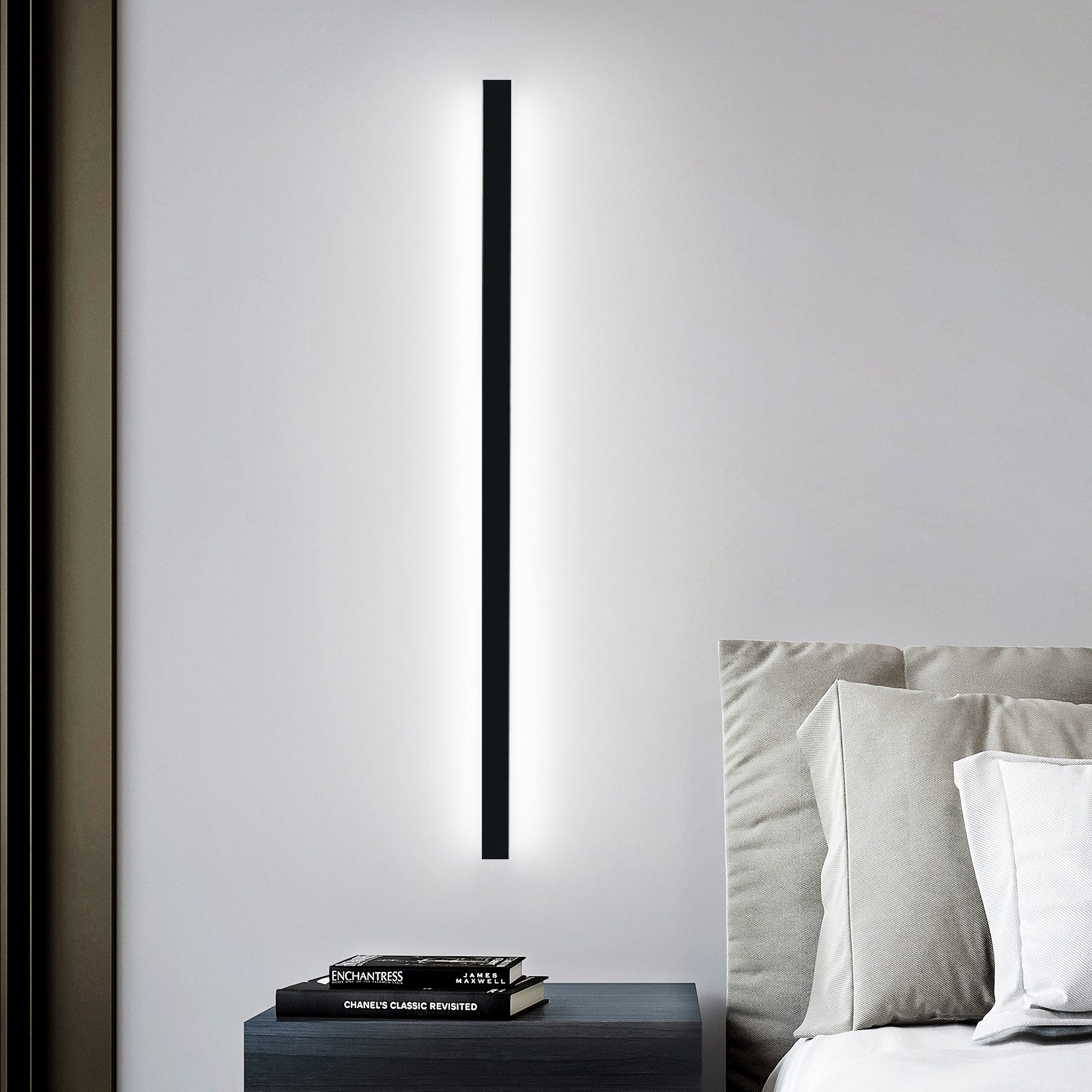 Applique da parete. Una luce alta e verticale con cornice nera su un muro grigio sopra un comodino.