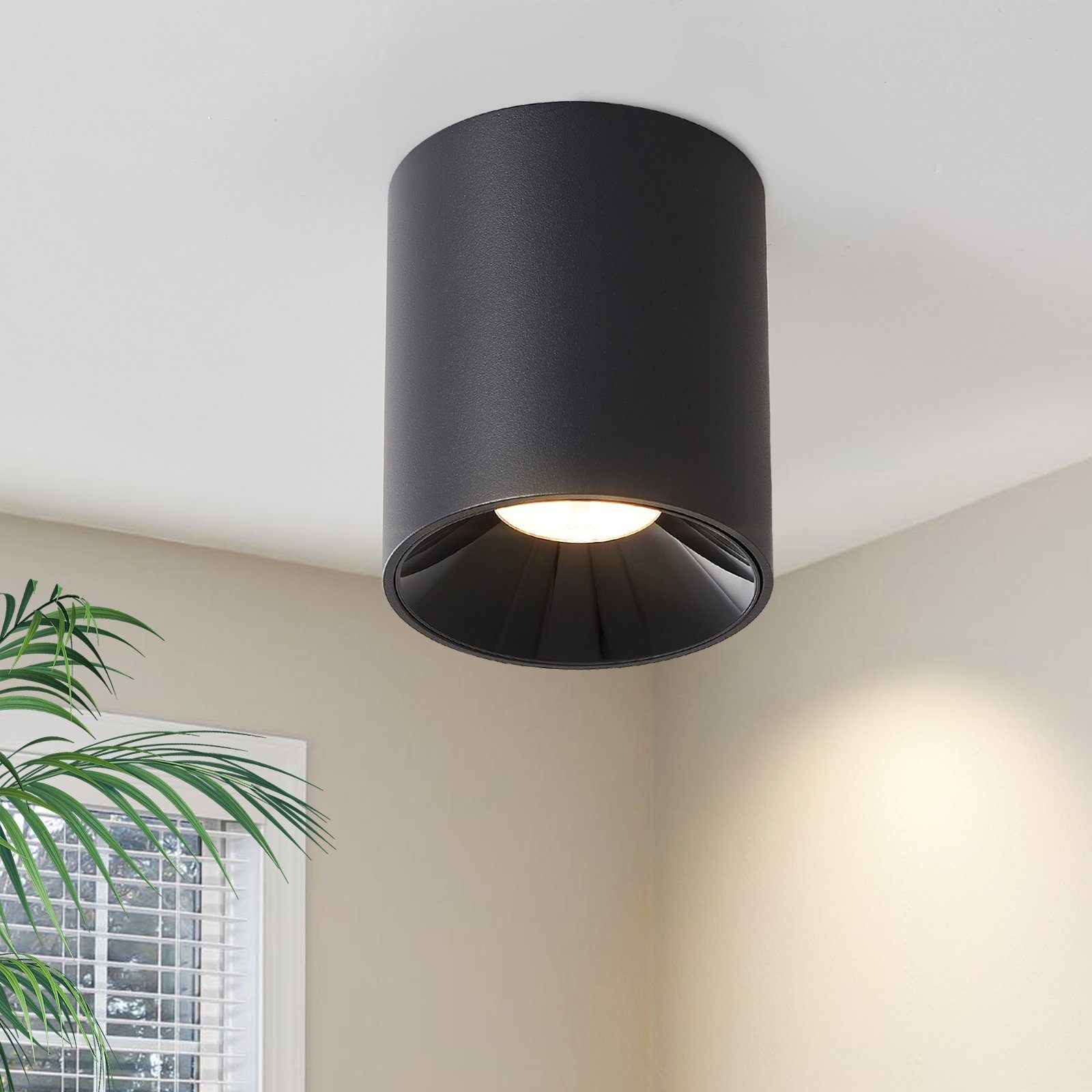 Lampada da soffitto cilindrica nera, illuminante. Sfondo: parete beige.