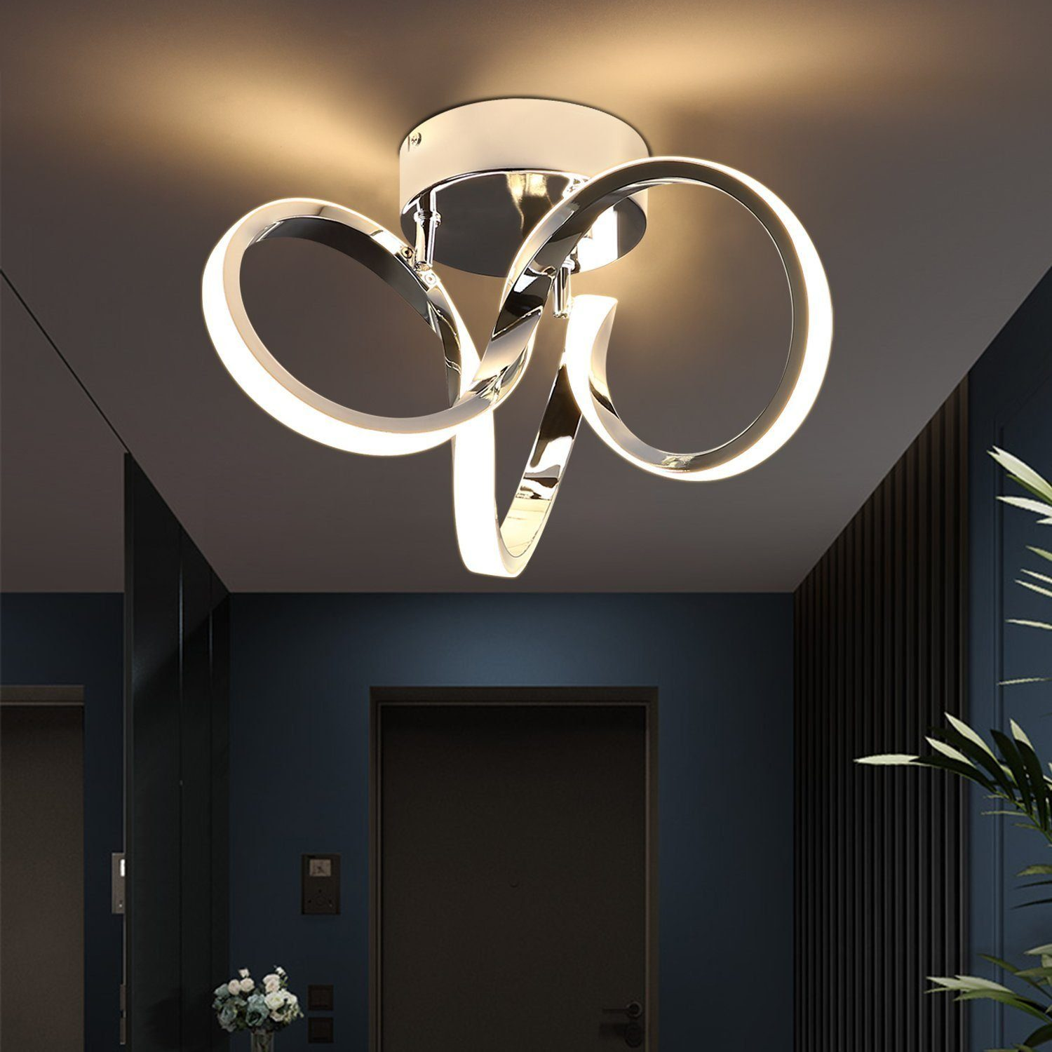 Lampada da soffitto cromata con tre elementi curvi e illuminati. Sfondo blu scuro.