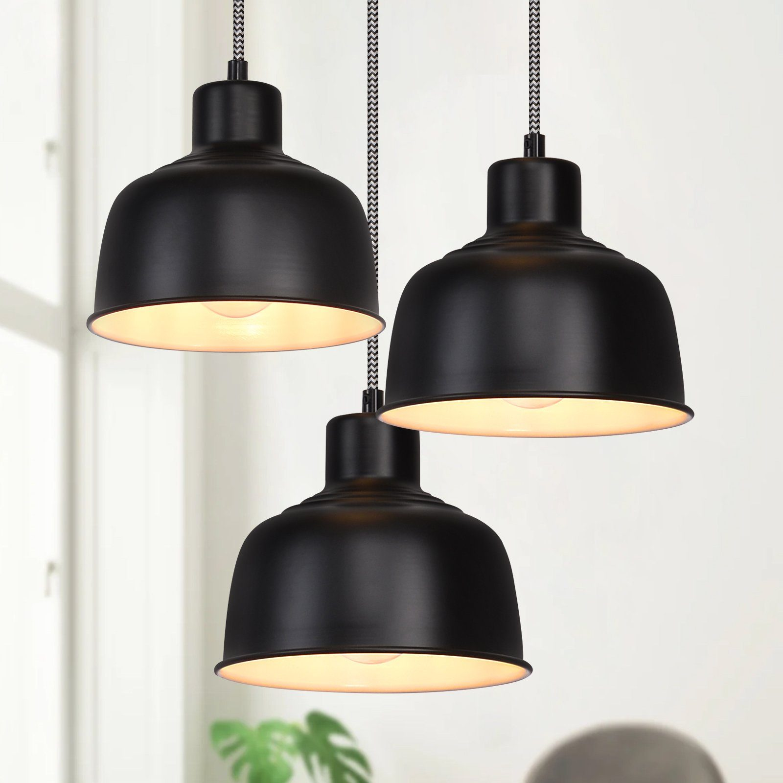 Tre lampade a sospensione nere con luce calda. Sono appese al soffitto con cavi bianchi e neri.