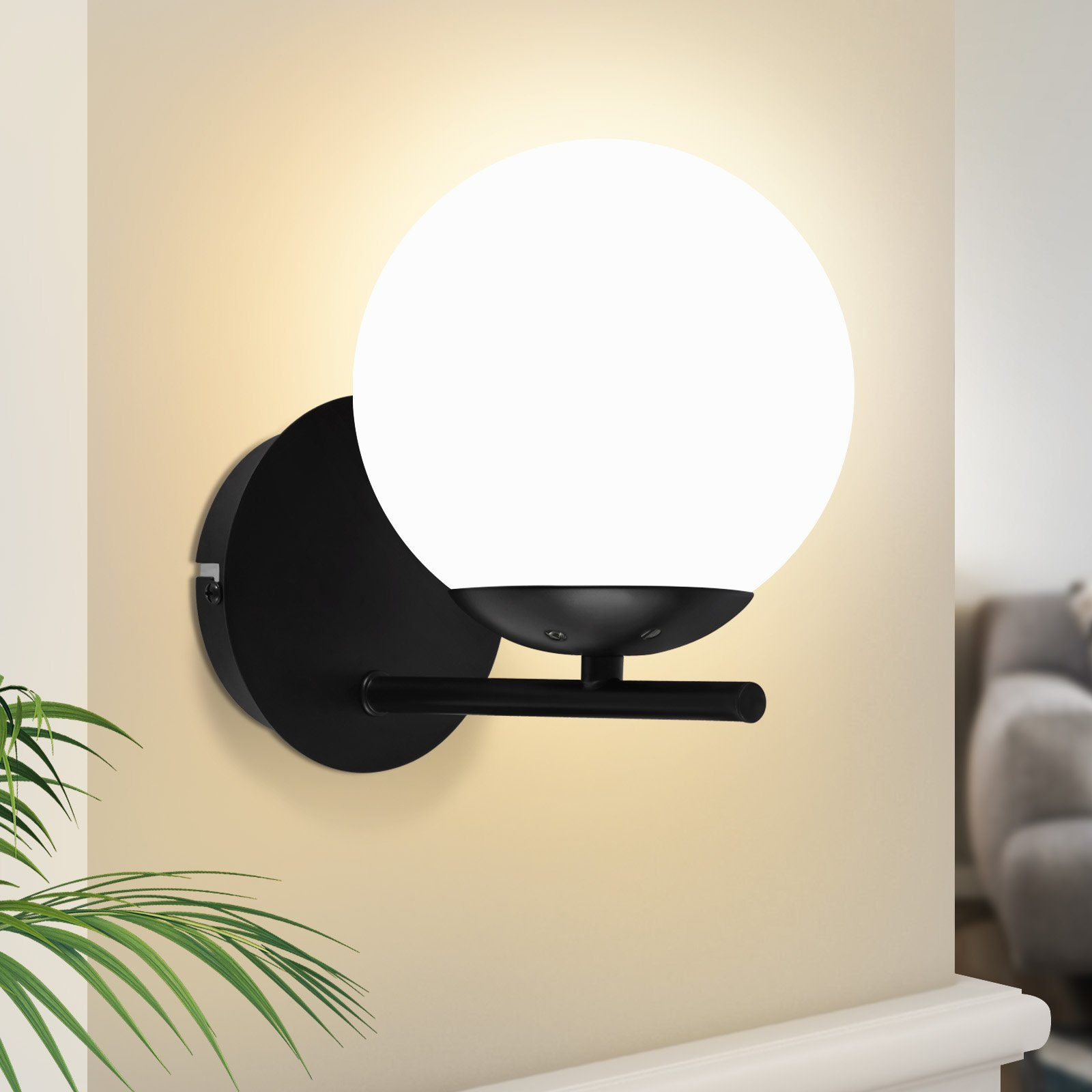Applique da parete nera con una luce bianca a forma di globo, montata su una parete chiara.