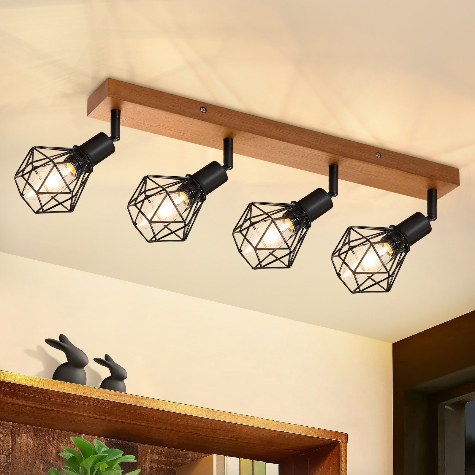 Quattro faretti neri su una trave di legno. Le luci sono rivolte verso il basso. Ci sono conigli decorativi sotto di loro.
