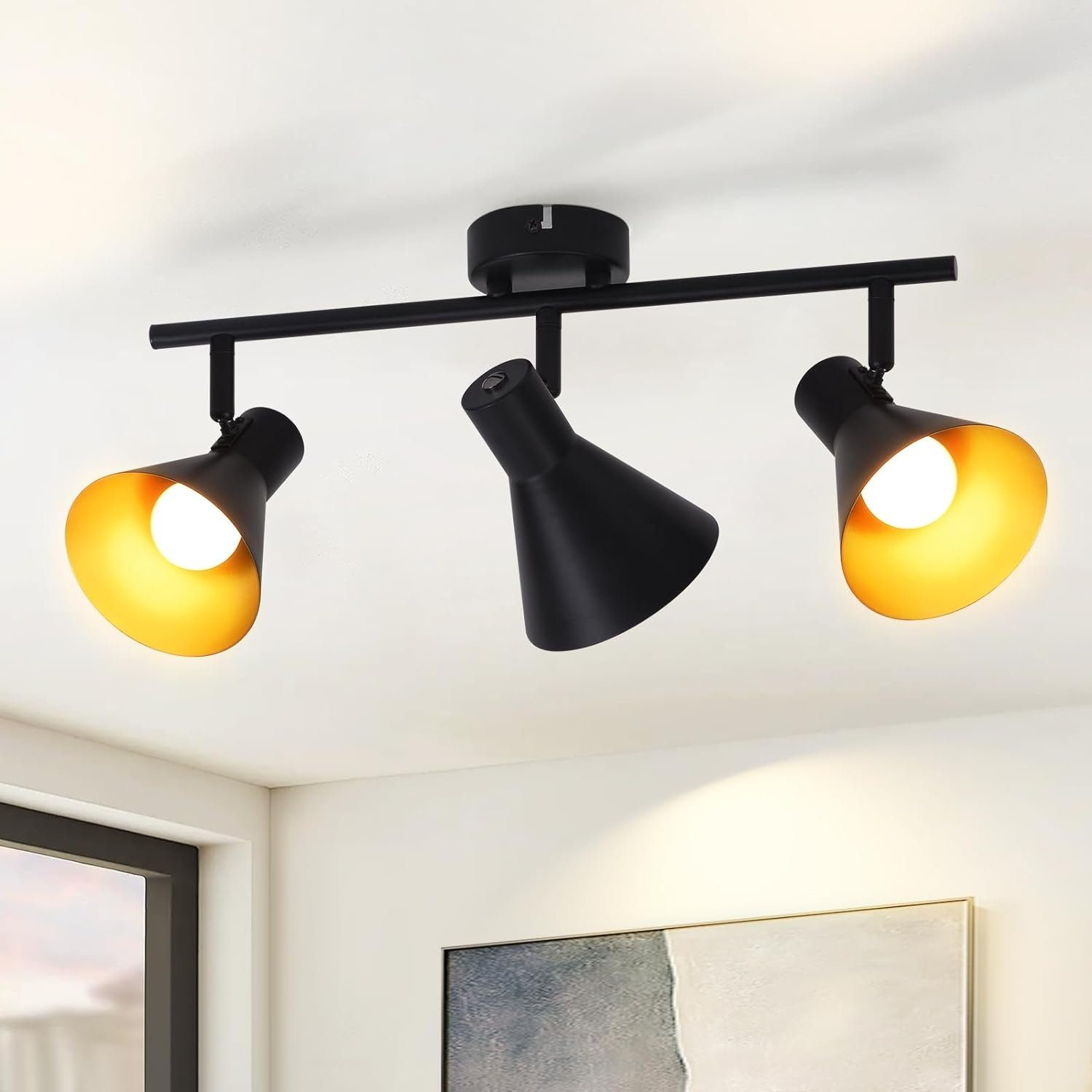 Faretto da soffitto nero con tre lampade regolabili, ognuna con rivestimento interno dorato.