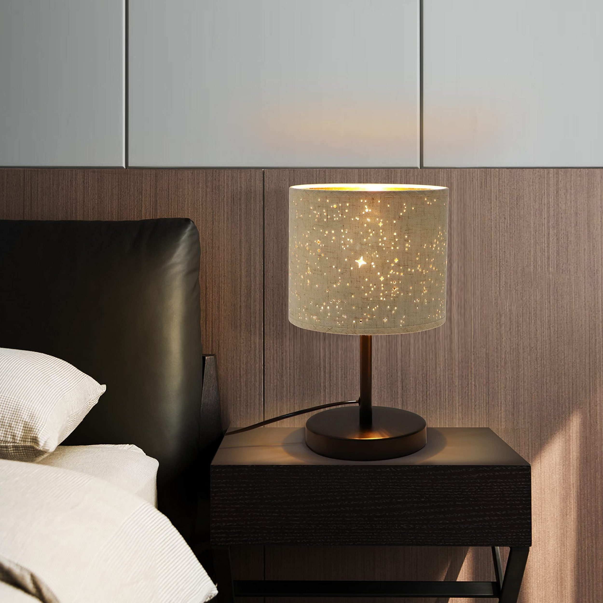 Podświetlana lampka nocna z kloszem w kształcie gwiazdy. Lampa stoi na ciemnej szafce nocnej.