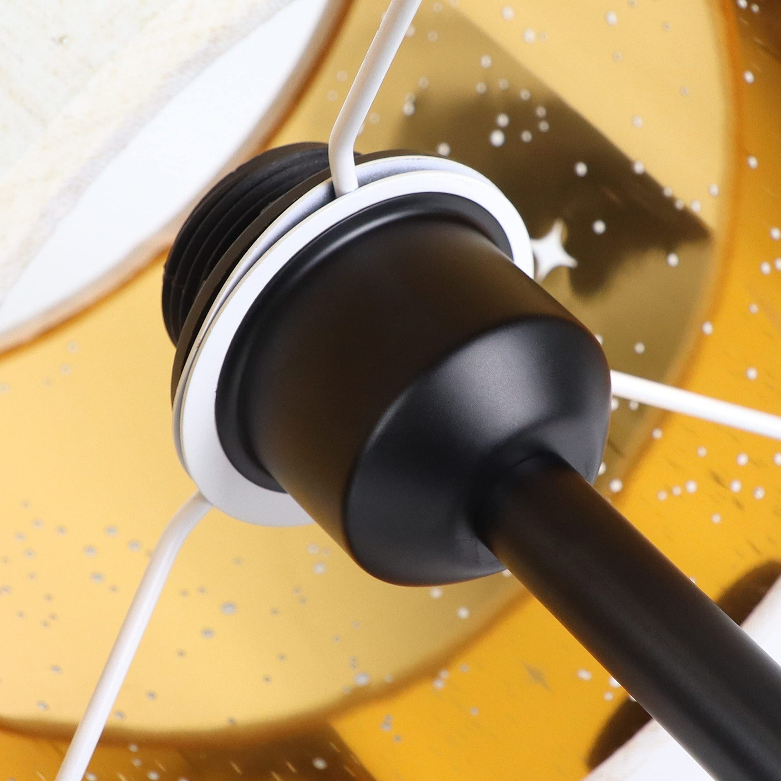 Zbliżenie czarnej części lampy z białym okablowaniem na złotym tle.