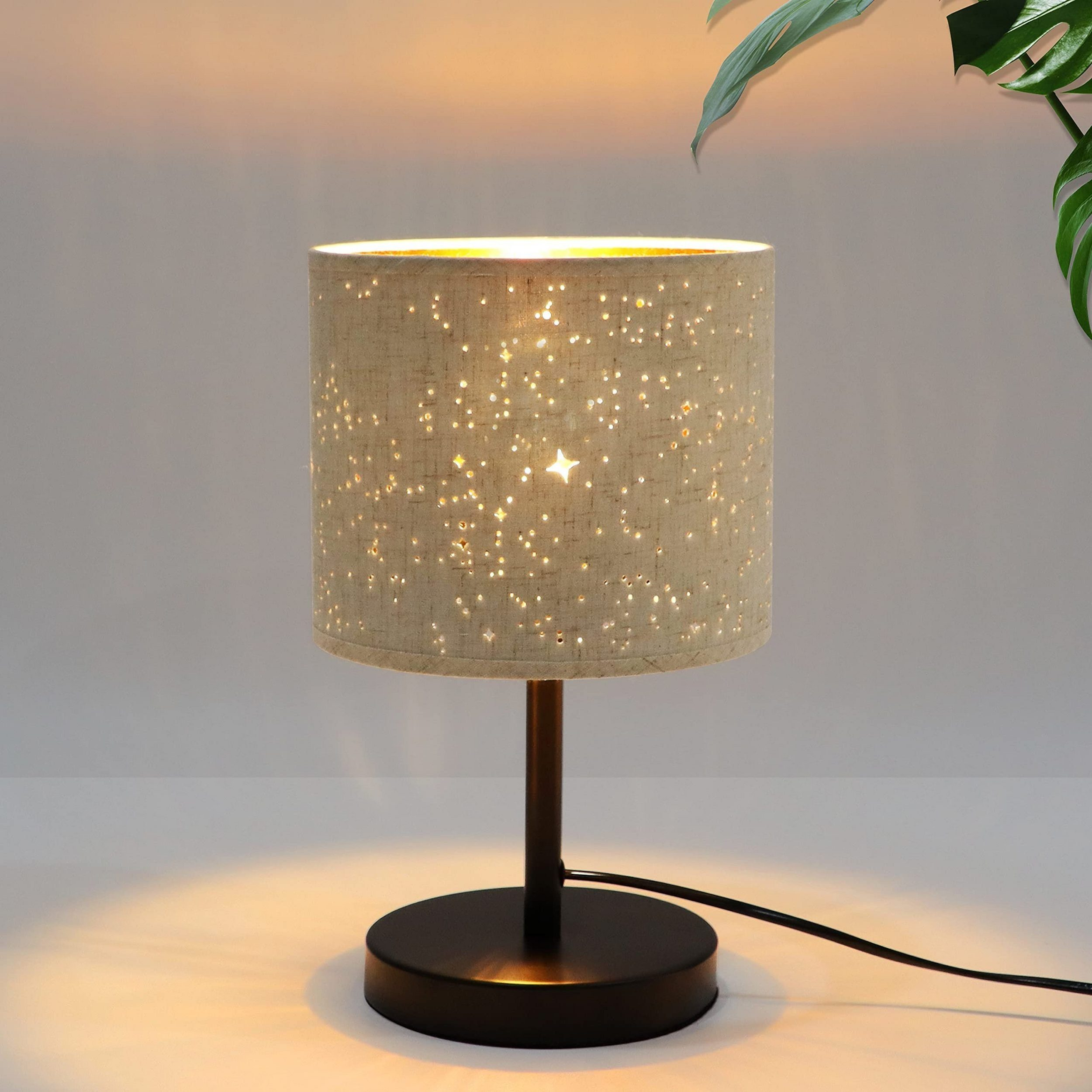 Lampa stołowa z kloszem w kształcie gwiazdy. Lampa jest włączona. Podstawa jest czarna.