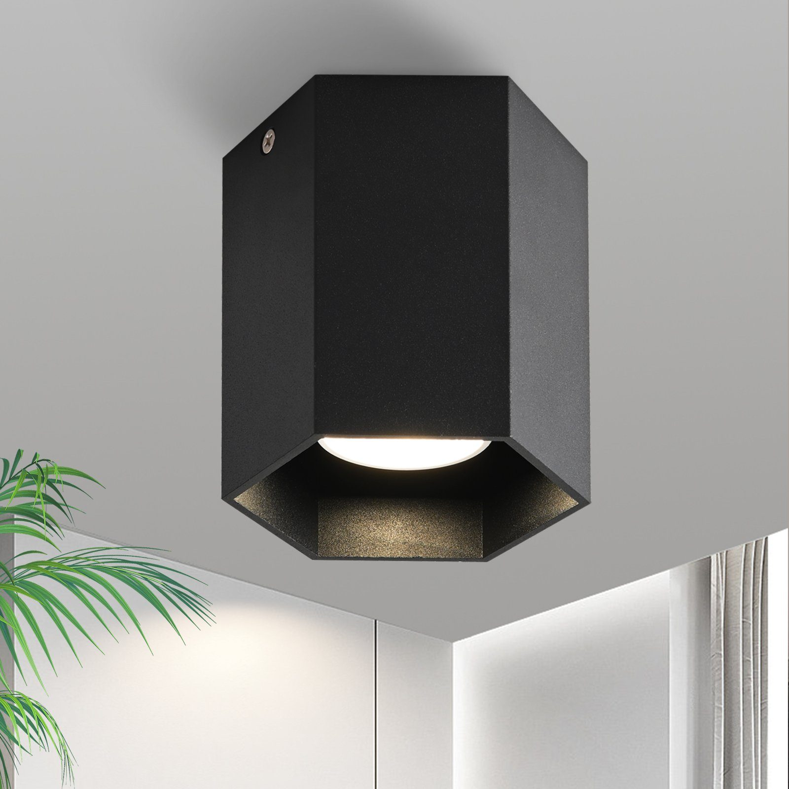 Una plafoniera esagonale nera. La luce è accesa e illumina il soffitto.