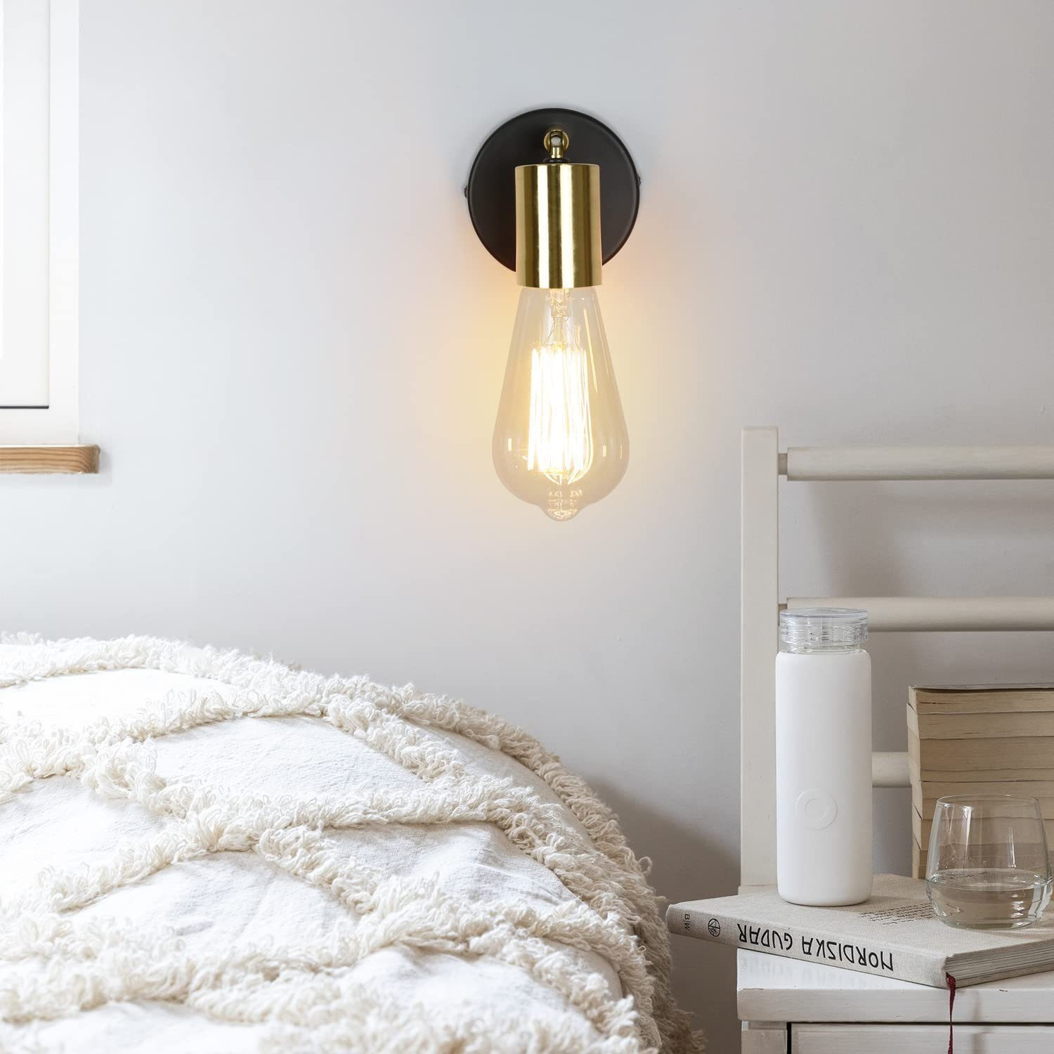Lampada da parete con base nera e dettagli dorati, accanto a un letto.