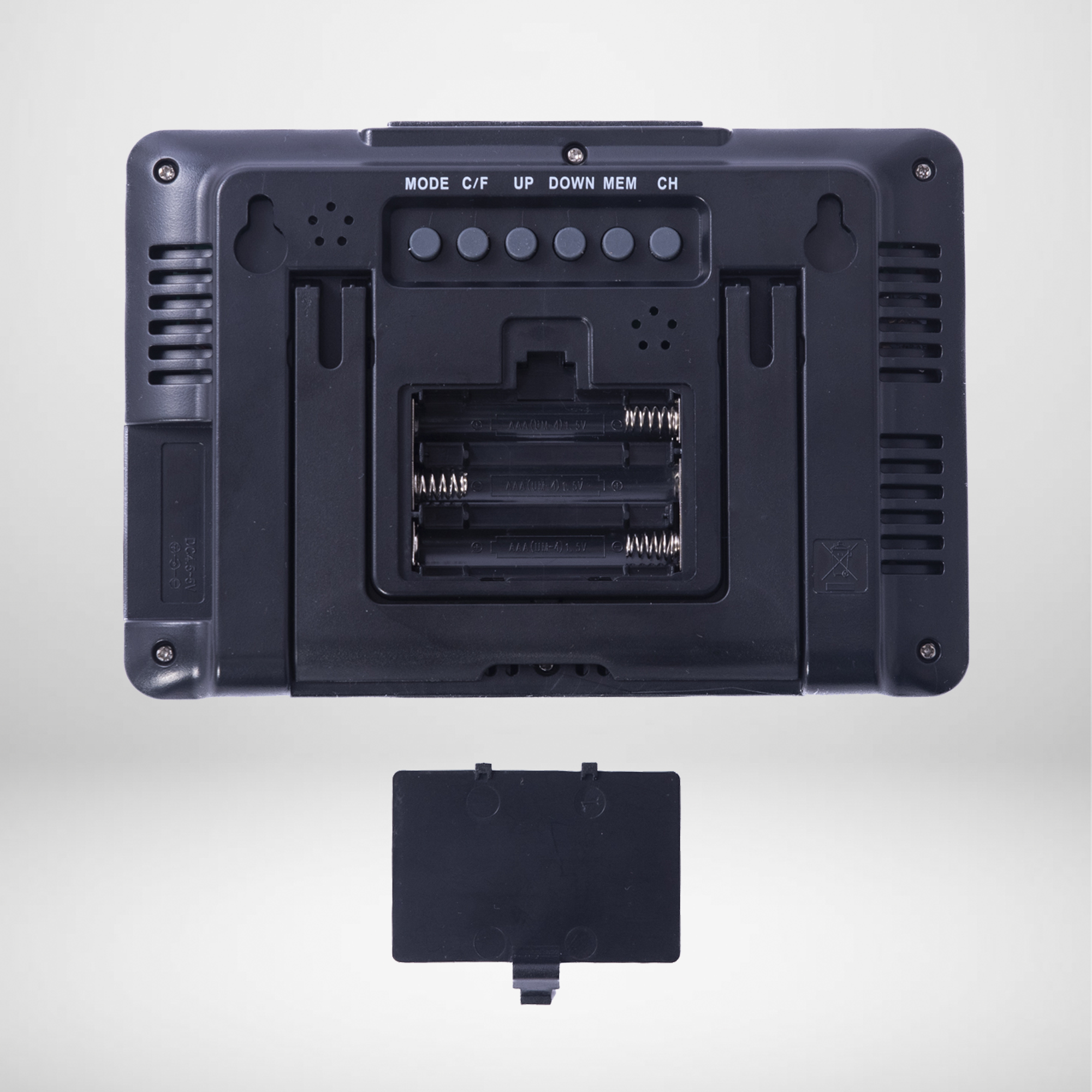 Tył czarnego zegara cyfrowego z widocznymi w środku bateriami. Pokrywa baterii jest częściowo zdjęta.