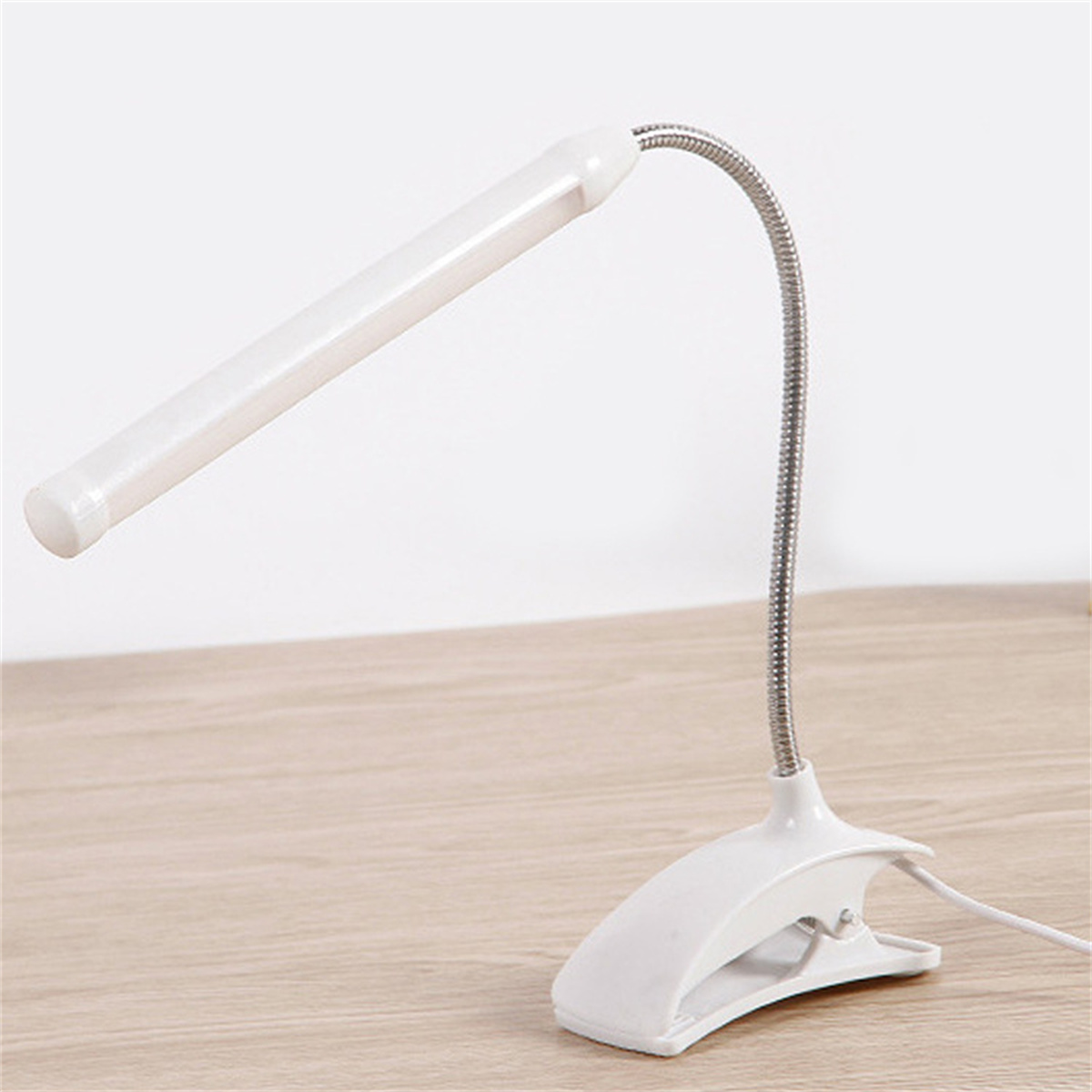 Eine weiße Schreibtischlampe mit flexiblem Hals und Clip-On-Basis. Sie steht auf einem Holzschreibtisch.