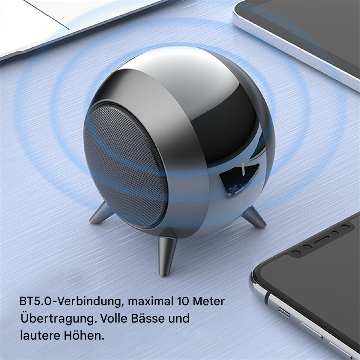 Ein silberner, runder Lautsprecher mit drei Beinen, Lautstärkeregler und einem schwarzen Telefon auf weißer Oberfläche.