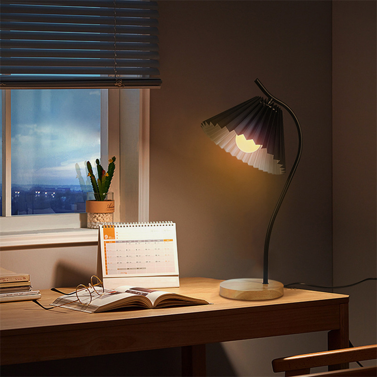 Schreibtisch mit Lampe, Kalender, Buch und Brille am Fenster.